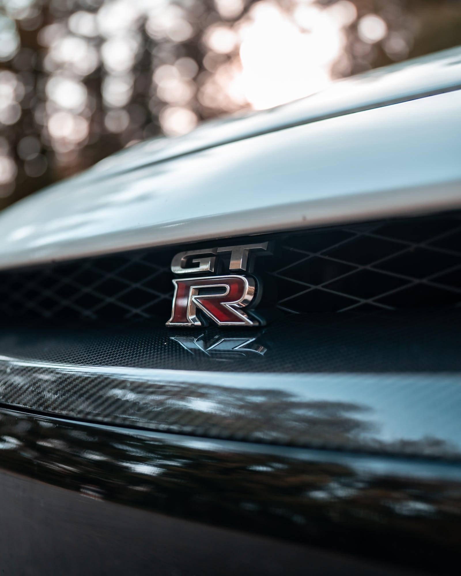 日產 桌布 壁紙 — 近距離拍攝閃亮的GT-R徽章，位於時尚跑車引擎蓋上，背景為模糊的森林。