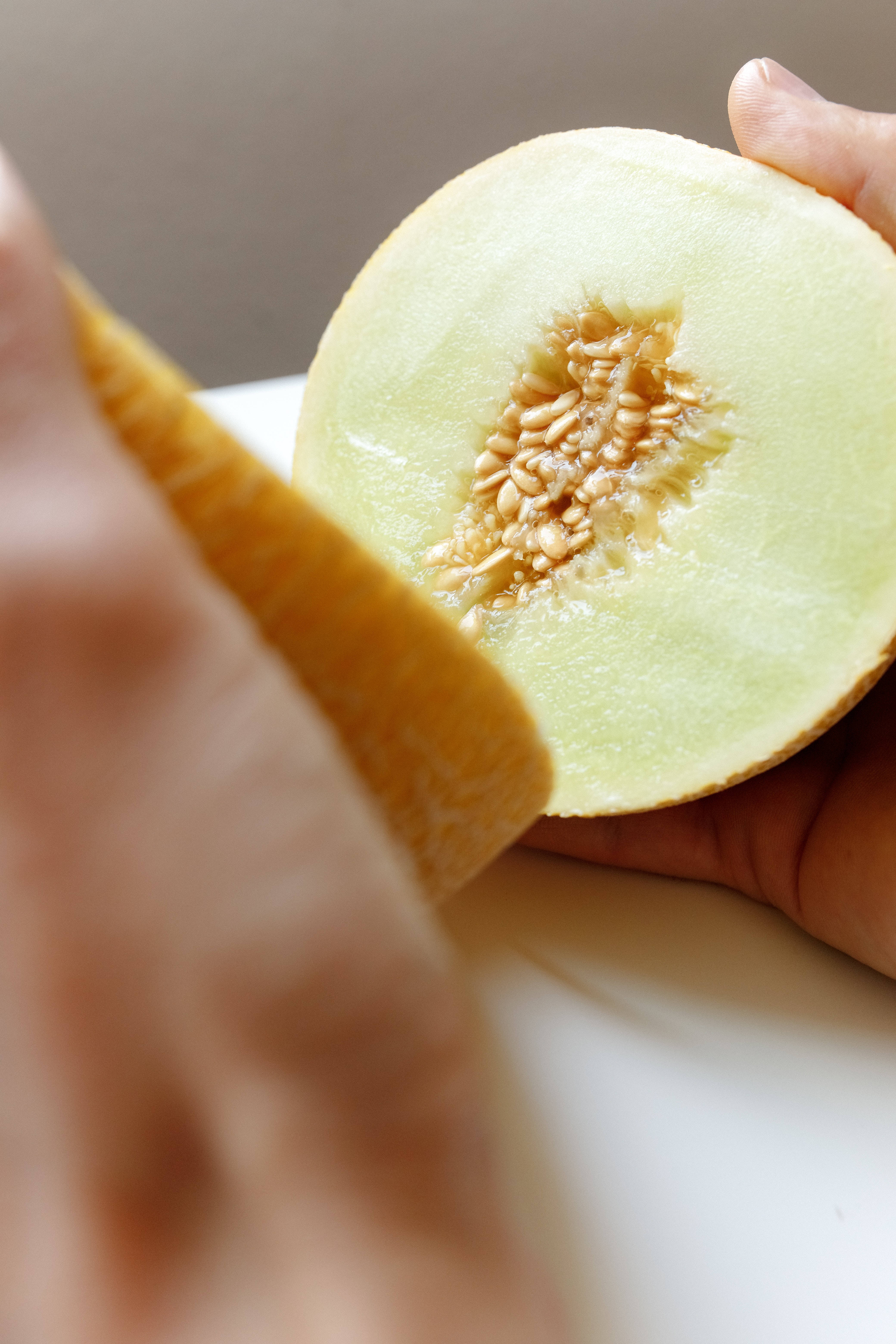Fruits 桌布 壁紙 — 近距離拍攝雙手切開新鮮蜜瓜，露出多汁的淡綠色果肉和種子。