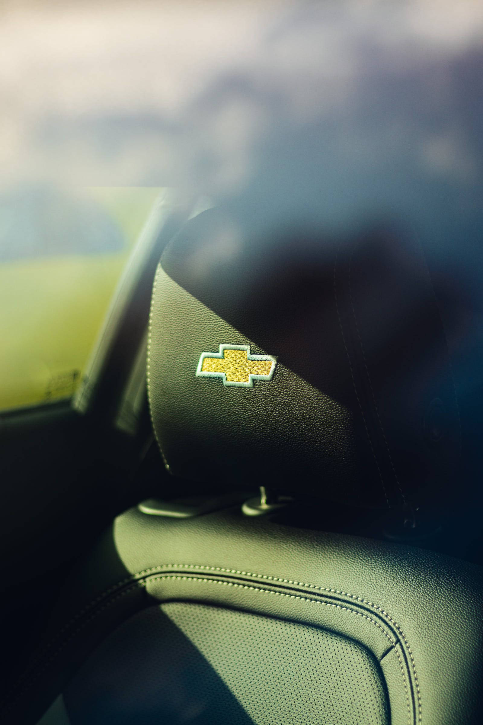 Chevrolet Logo 桌布 壁紙 — 近距離拍攝雪佛蘭標誌刺繡在黑色皮革汽車頭枕上，陽光投射出陰影。