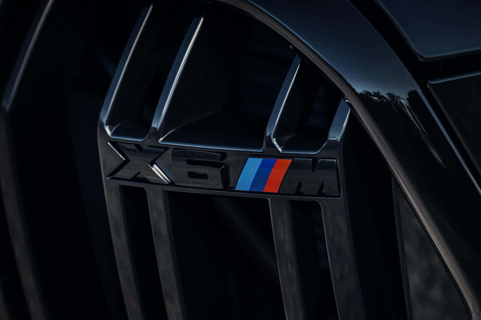 BMW X6 M 桌布 壁紙 — 近距離拍攝黑色BMW X6M水箱護罩徽章，帶有藍、紅、紫條紋，在戲劇性燈光下呈現。