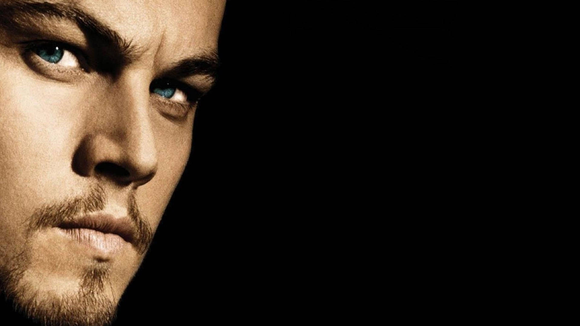 Dicaprio 桌布 壁紙 — 近距離肖像，一個男人擁有強烈的藍眼睛和鬍渣，背景是純黑色。