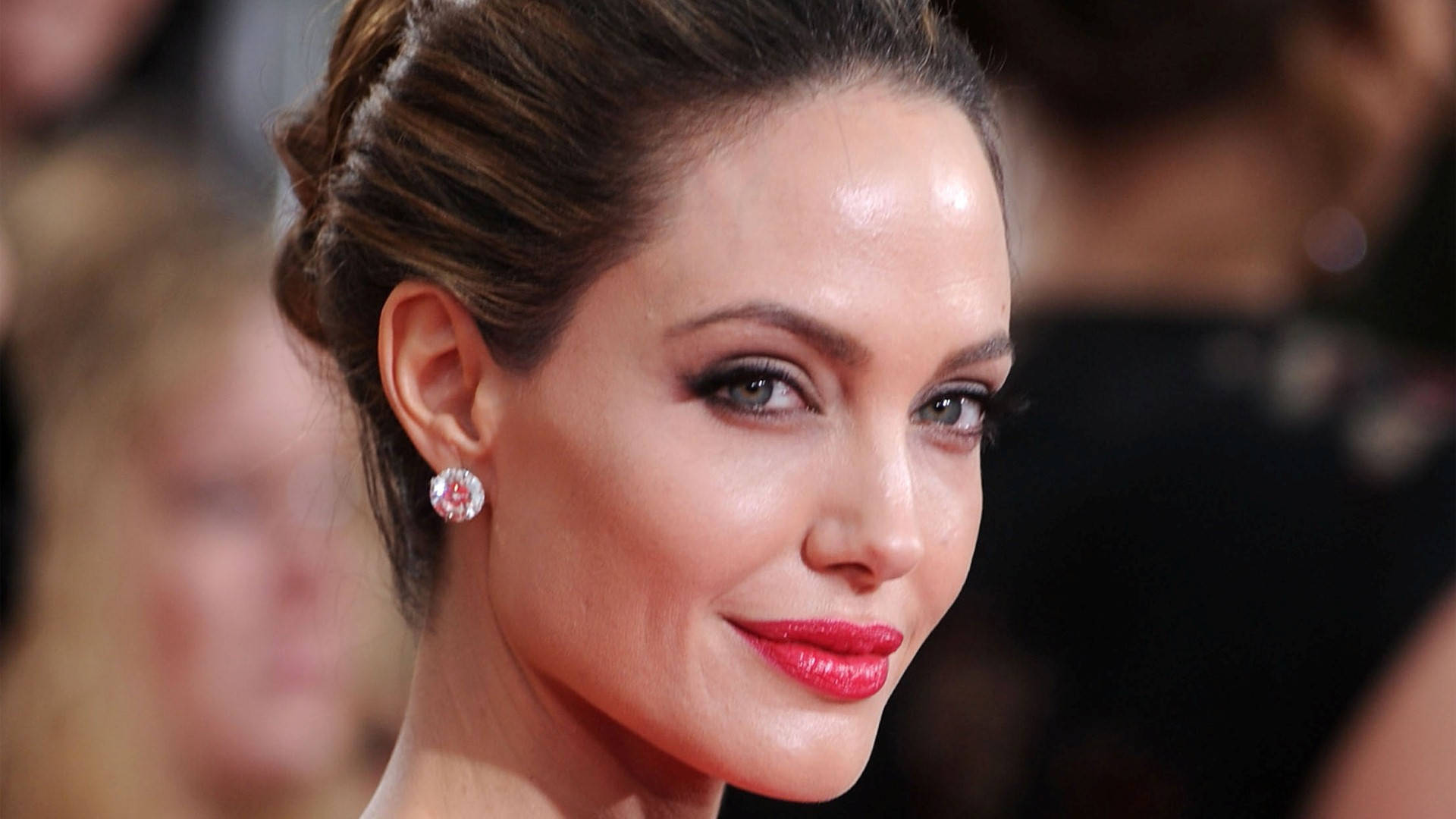Angelina 桌布 壁紙 — 近距離肖像照，一位女士梳著優雅的盤髮，塗著紅色唇膏，戴著閃爍的耳環，在一個華麗的活動中。