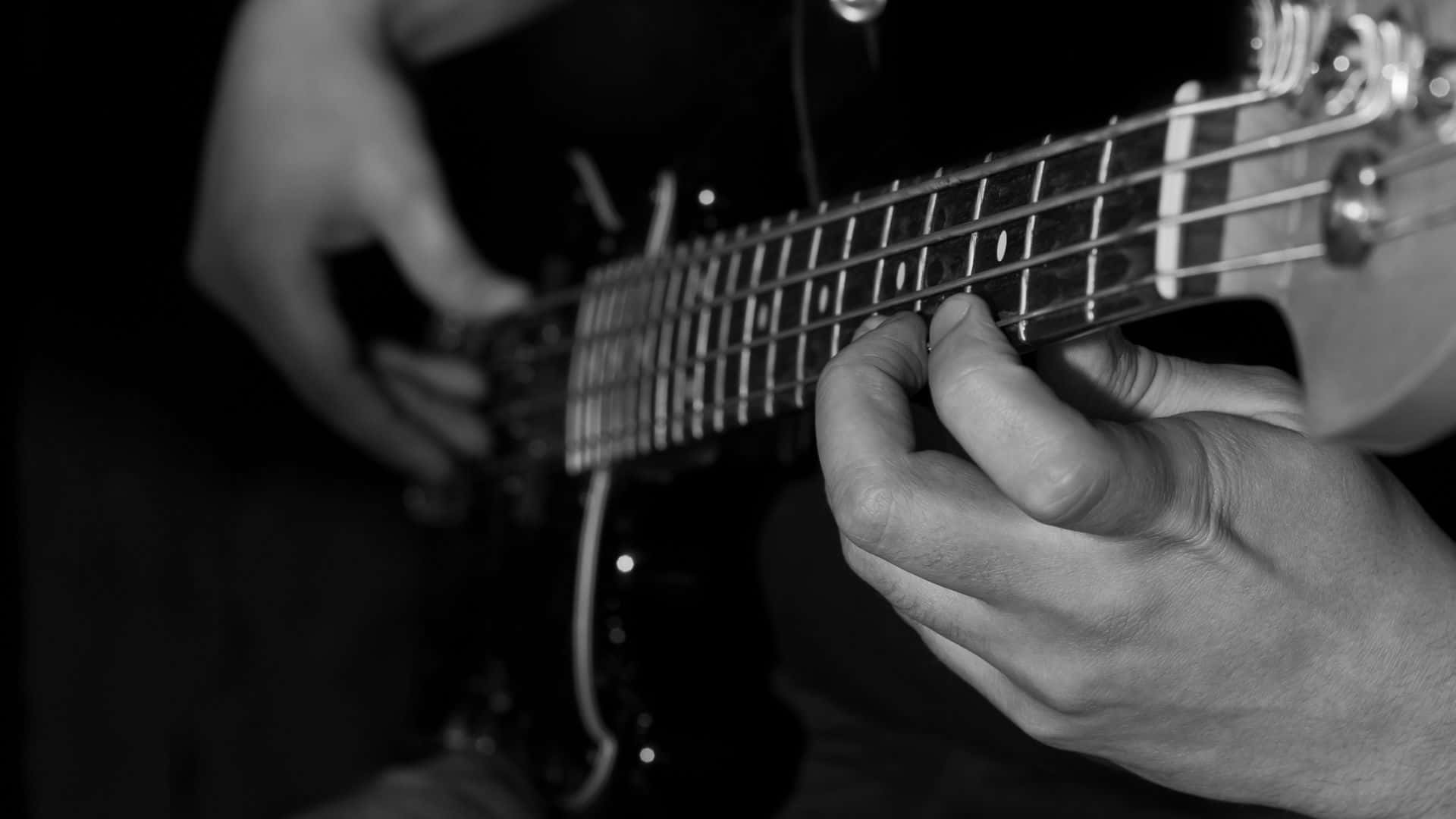 Black And White Guitar 桌布 壁紙 — 近距離黑白拍攝，雙手熟練地彈奏電吉他，充滿專注的強度。
