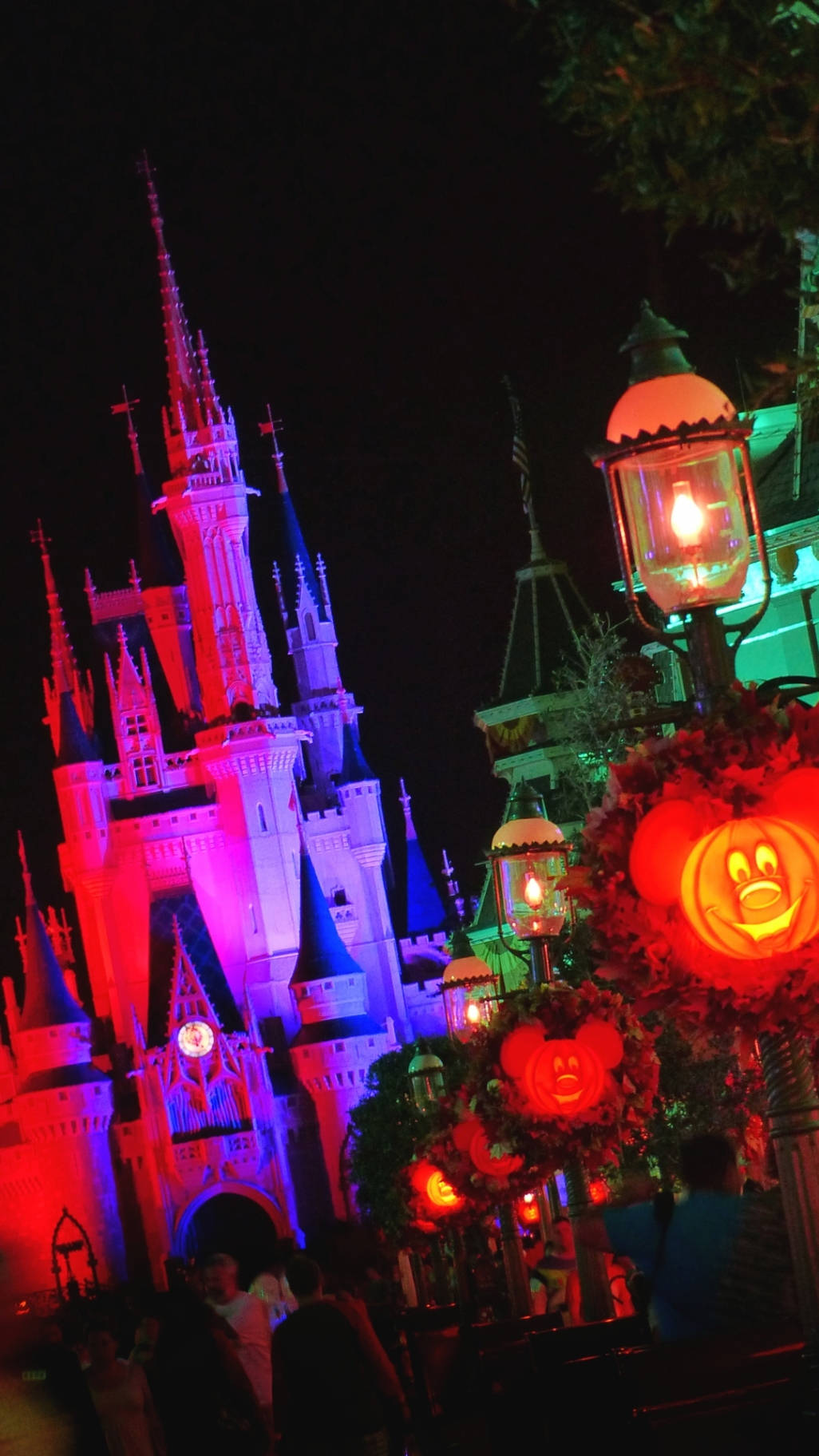 Disney Castle 桌布 壁紙 — 迪士尼城堡在夜晚被鮮豔的紫色和粉紅色燈光照亮，閃爍的南瓜燈和燈籠。