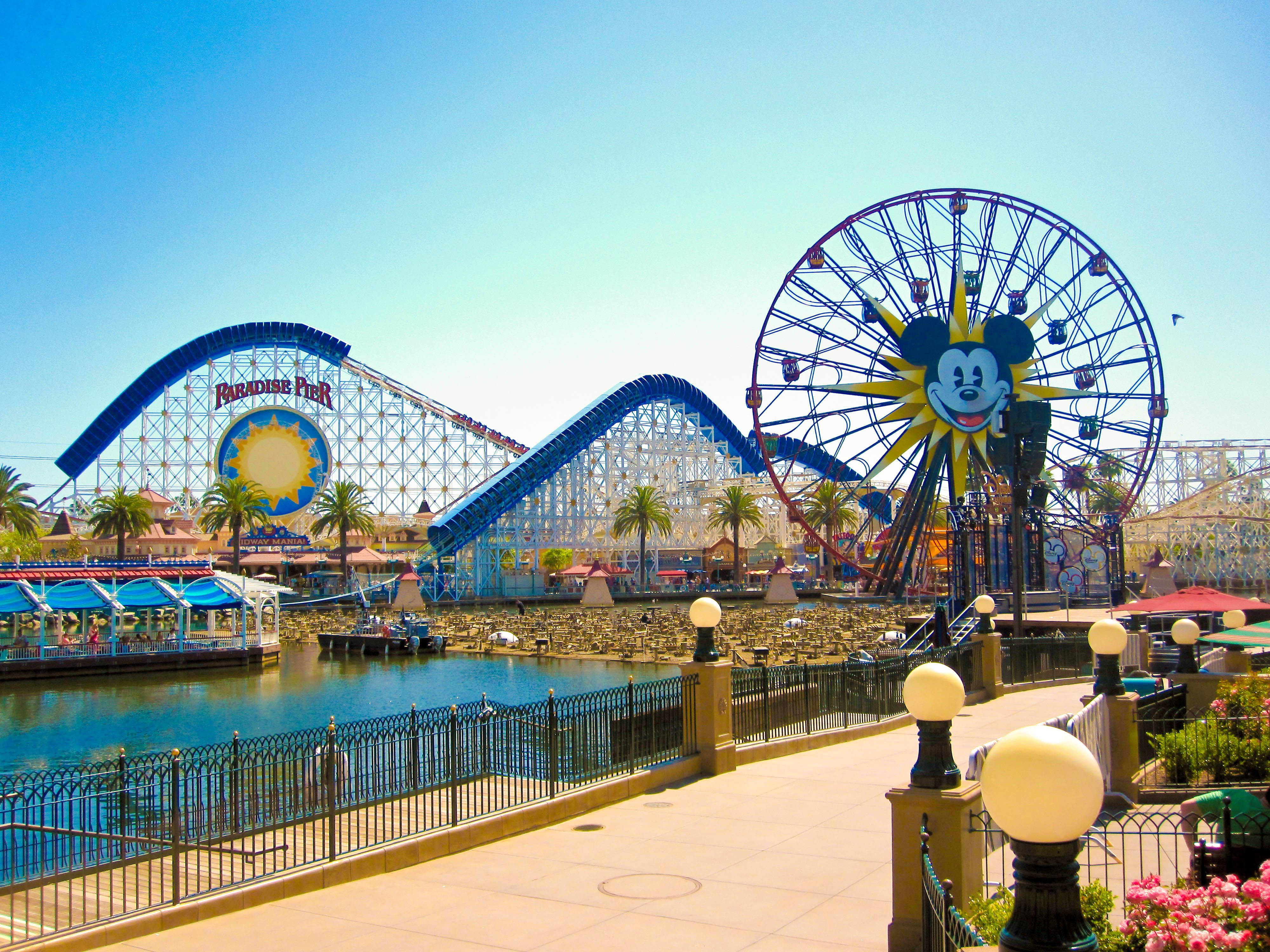 Theme Park 桌布 壁紙 — 迪士尼樂園晴朗的一天，天堂碼頭雲霄飛車和米奇老鼠摩天輪俯瞰平靜的水道。