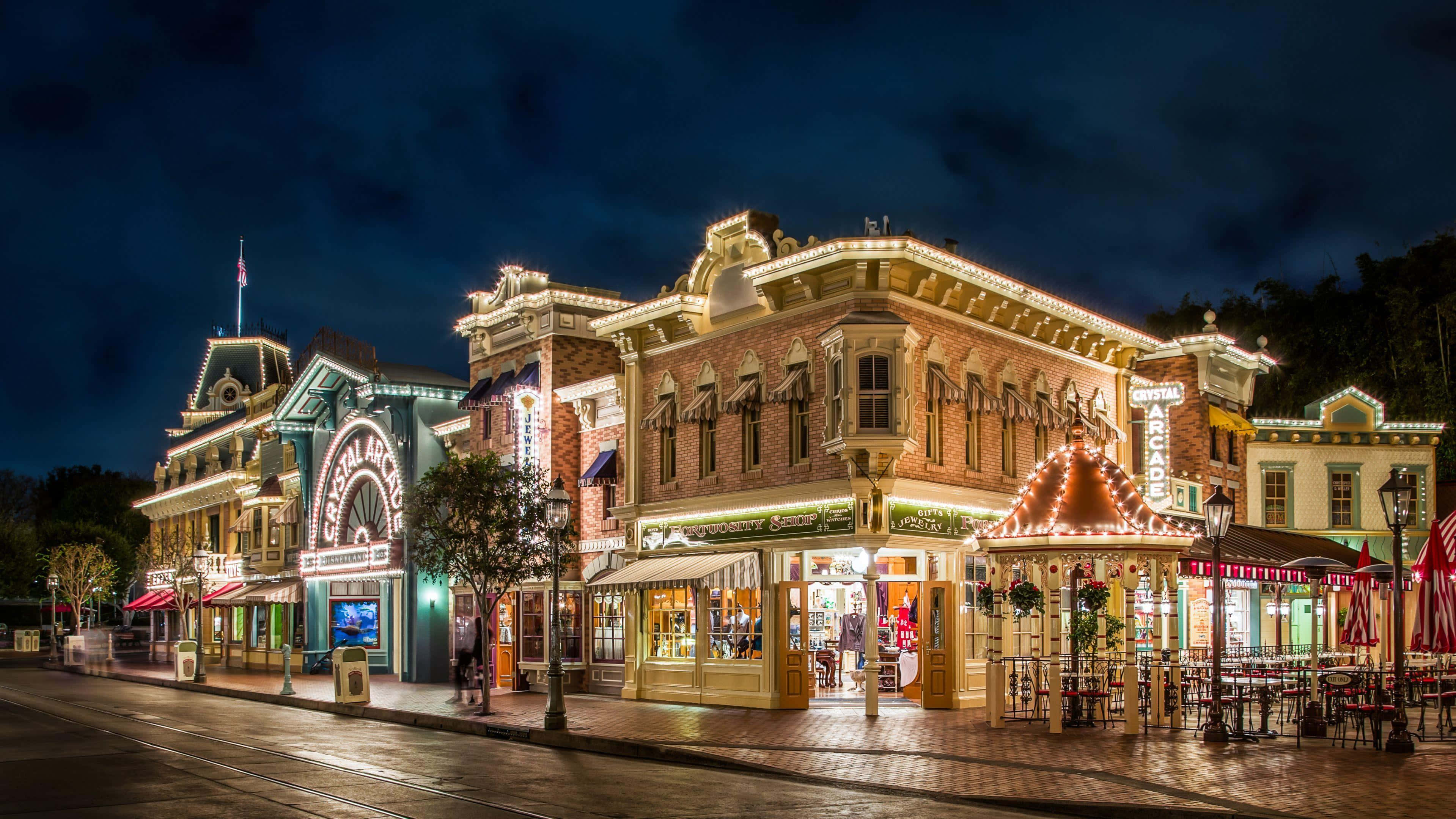 Disneyland 桌布 壁紙 — 迪士尼樂園美國小鎮大街在黑暗天空下被節日燈飾和發光的商店櫥窗照亮的充滿活力的夜間街景。