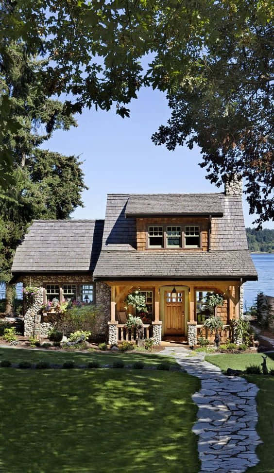 Cottage 桌布 壁紙 — 迷人的鄉村風格石木小屋，石徑通往門廊，俯瞰寧靜湖泊，四周綠樹成蔭，藍天白雲。