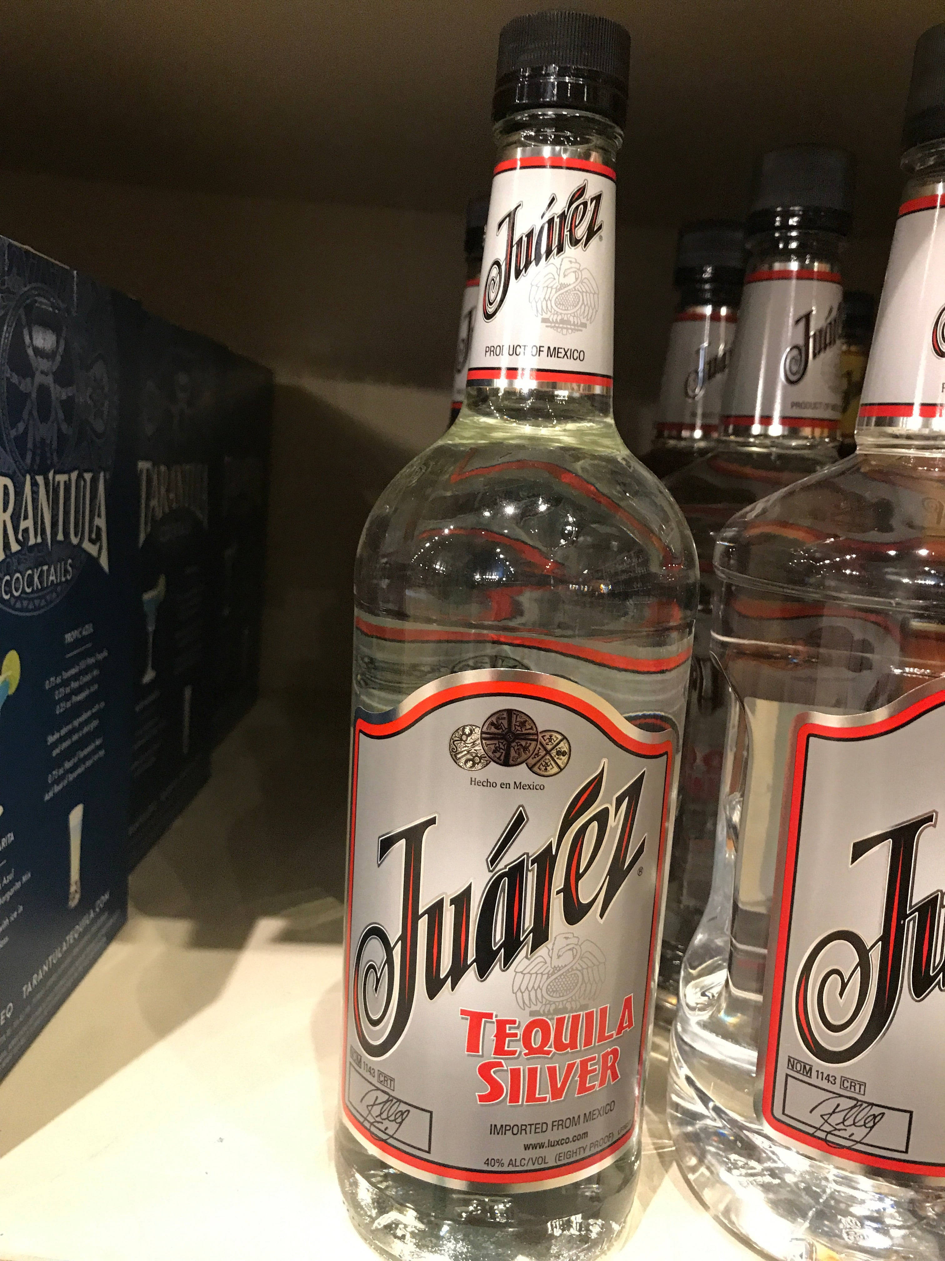 alcohol 桌布 壁紙 — 透明玻璃瓶的Juárez Tequila Silver整齊排列在架子上，背景有一個藍色雞尾酒盒。