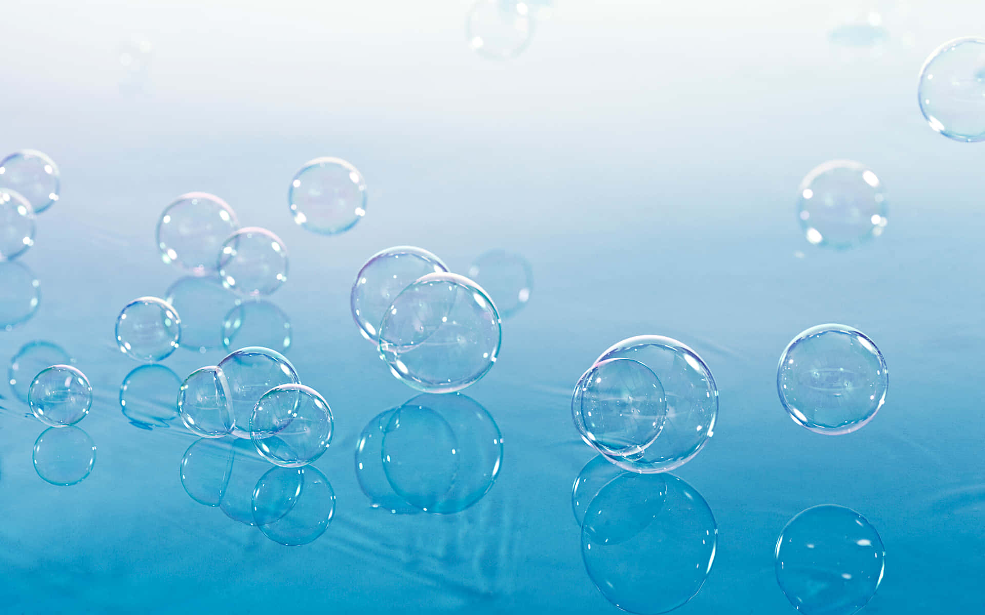 Bubbles 桌布 壁紙 — 透明肥皂泡在光滑的藍色表面上漂浮並反射，營造出寧靜而細膩的視覺效果。