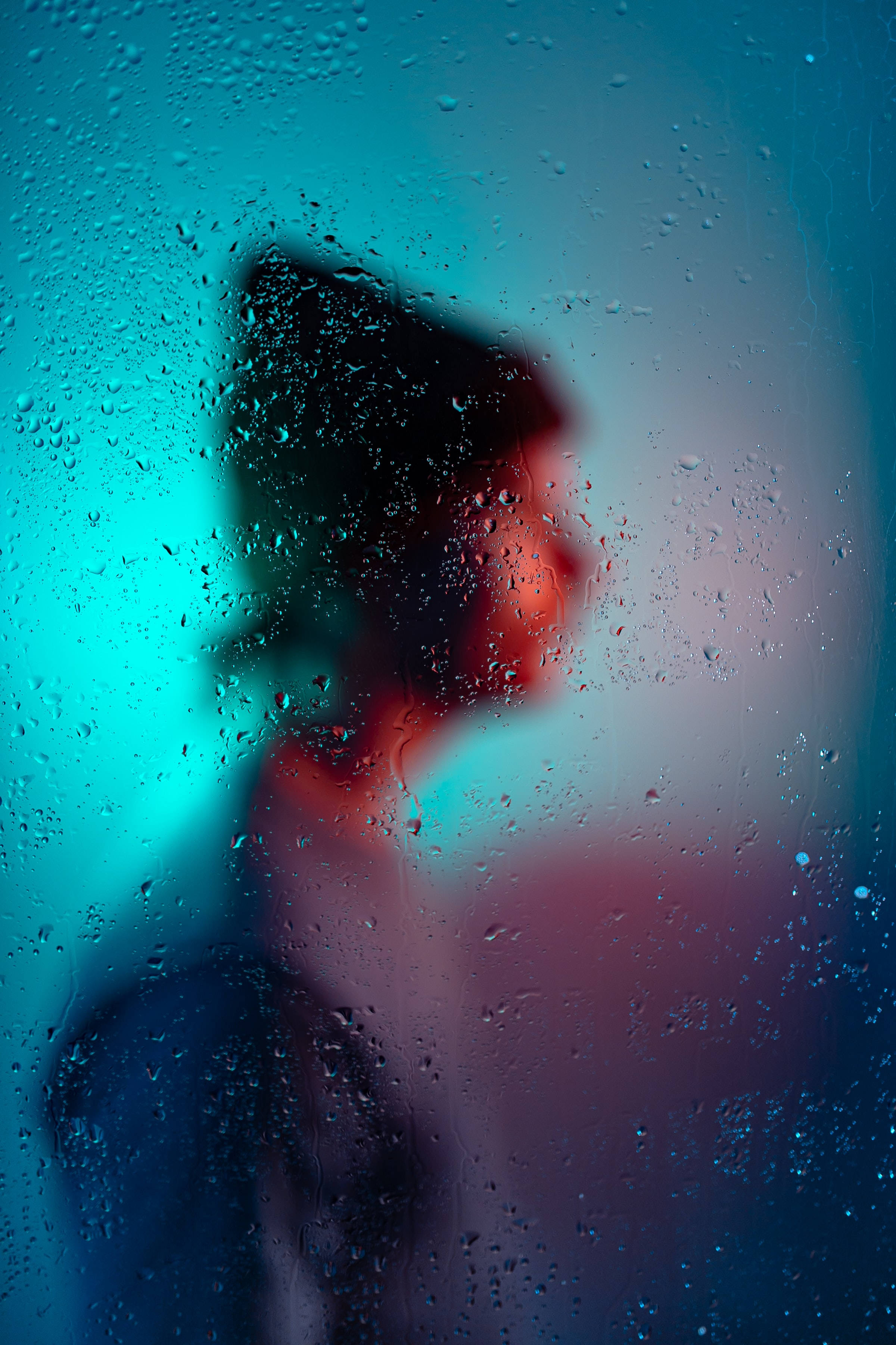 Man 桌布 壁紙 — 透過佈滿雨點的窗戶看到一個模糊的人影，散發著冷藍色和暖紅色的光芒。