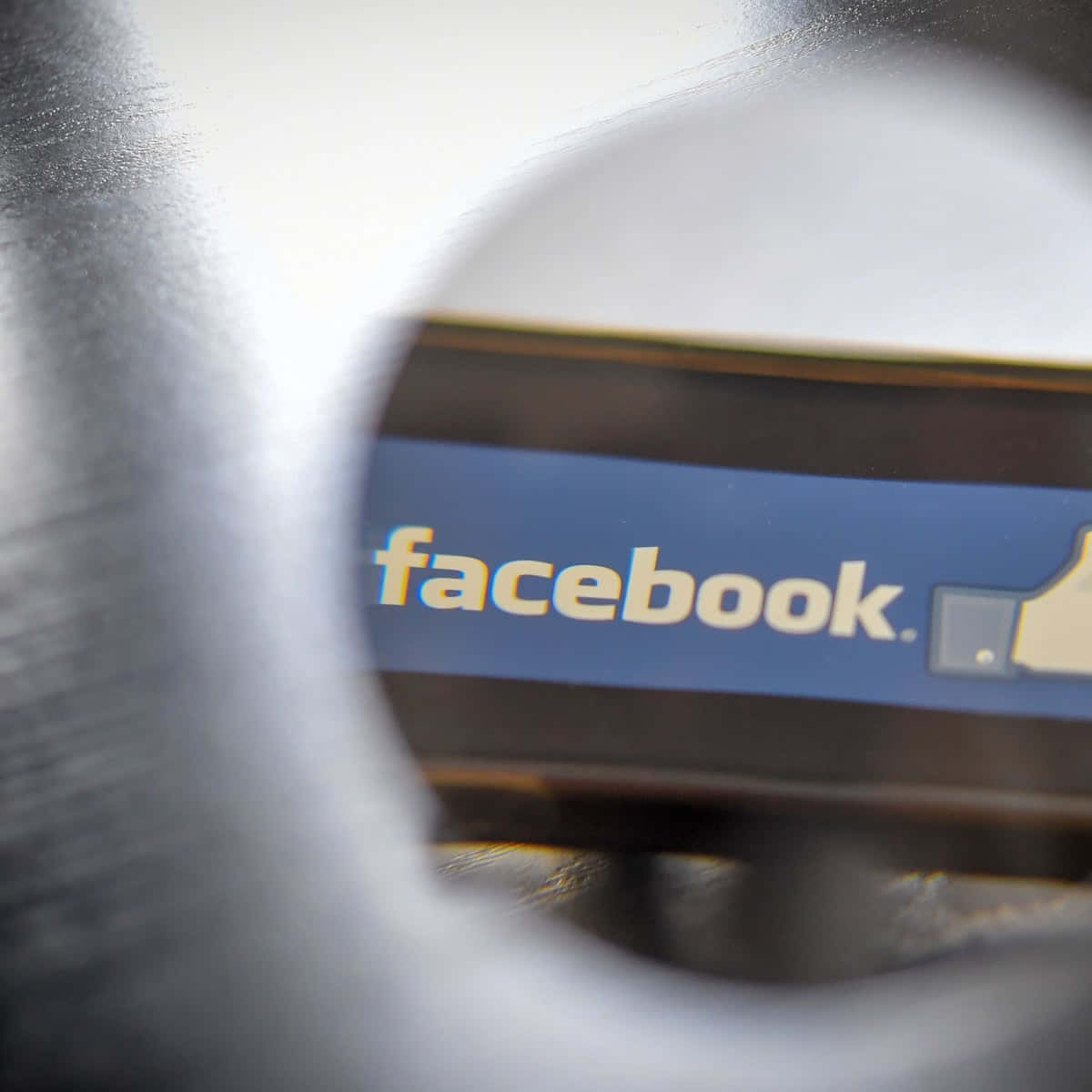 Facebook 桌布 壁紙 — 透過圓形開口看到的Facebook標誌特寫，周圍金屬模糊。