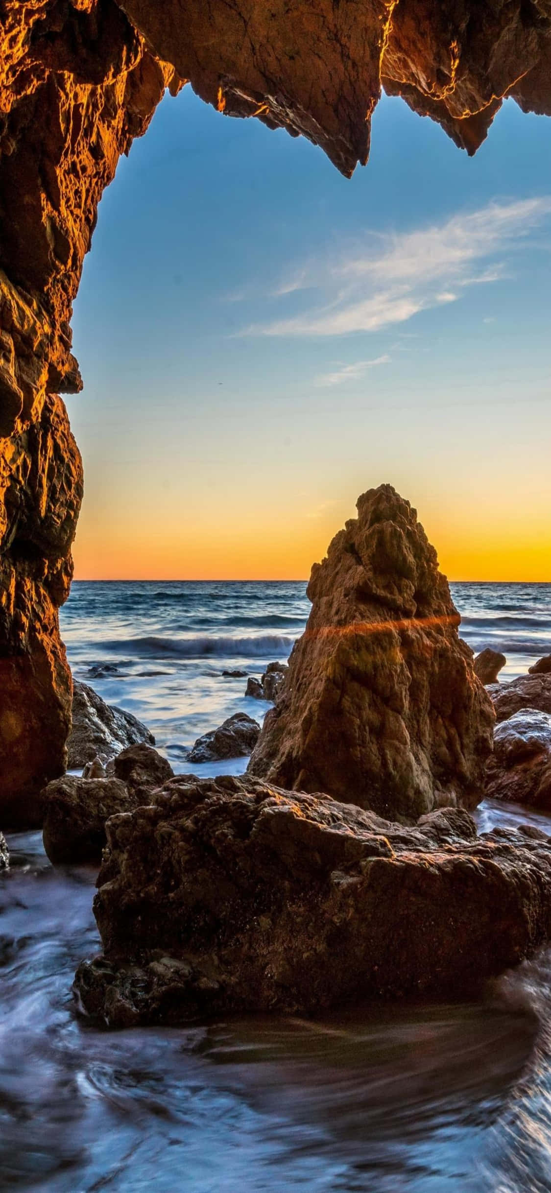 iPhone Xs Malibu 桌布 壁紙 — 透過天然岩石拱門觀賞日落，框住海浪和孤獨的海蝕柱。
