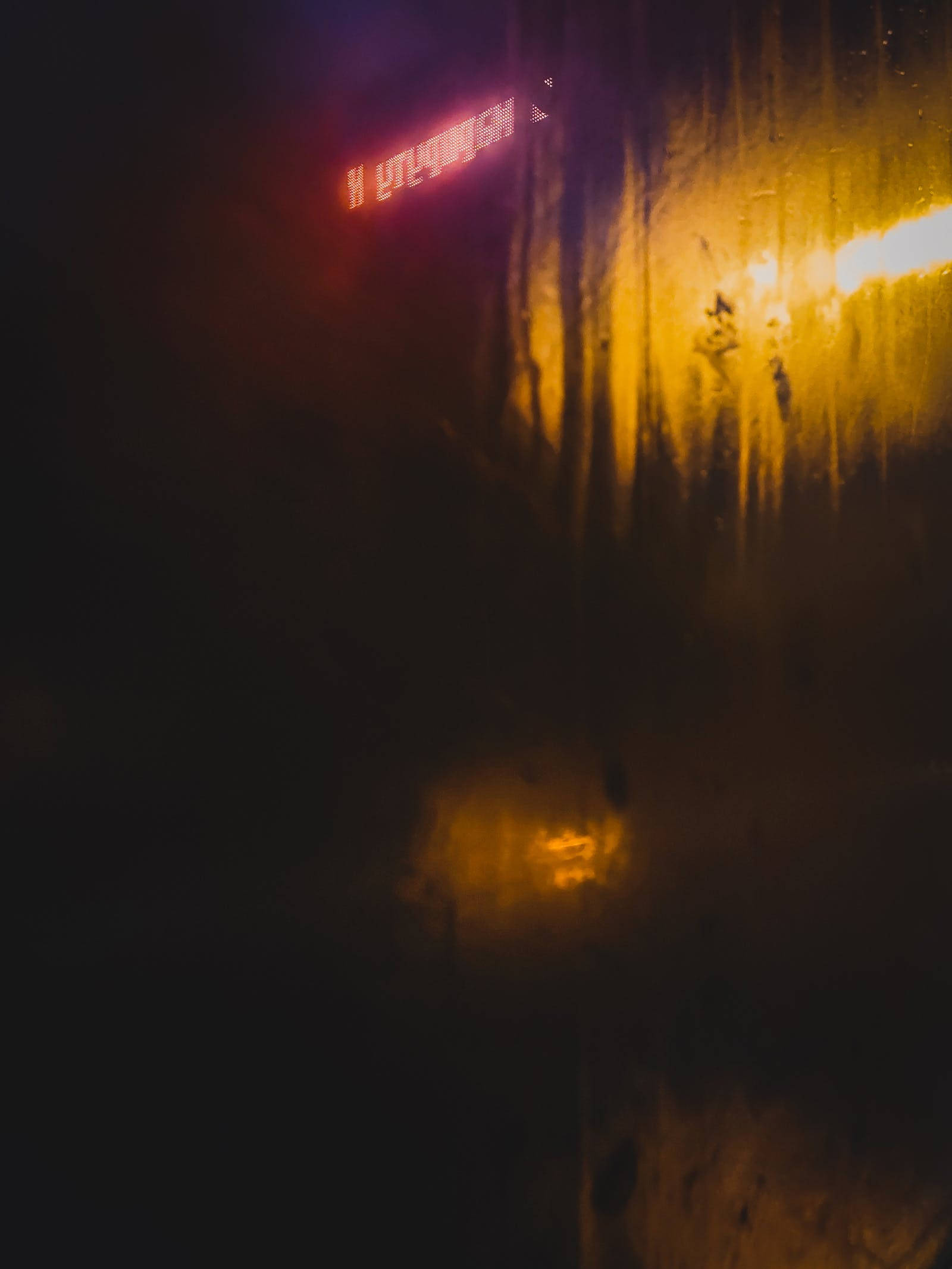 霓虹黃美學 桌布 壁紙 — 透過帶有雨痕的窗戶看到的雨夜景色，發光的霓虹招牌在黑暗中投射出溫暖的橙色和紅色光芒。
