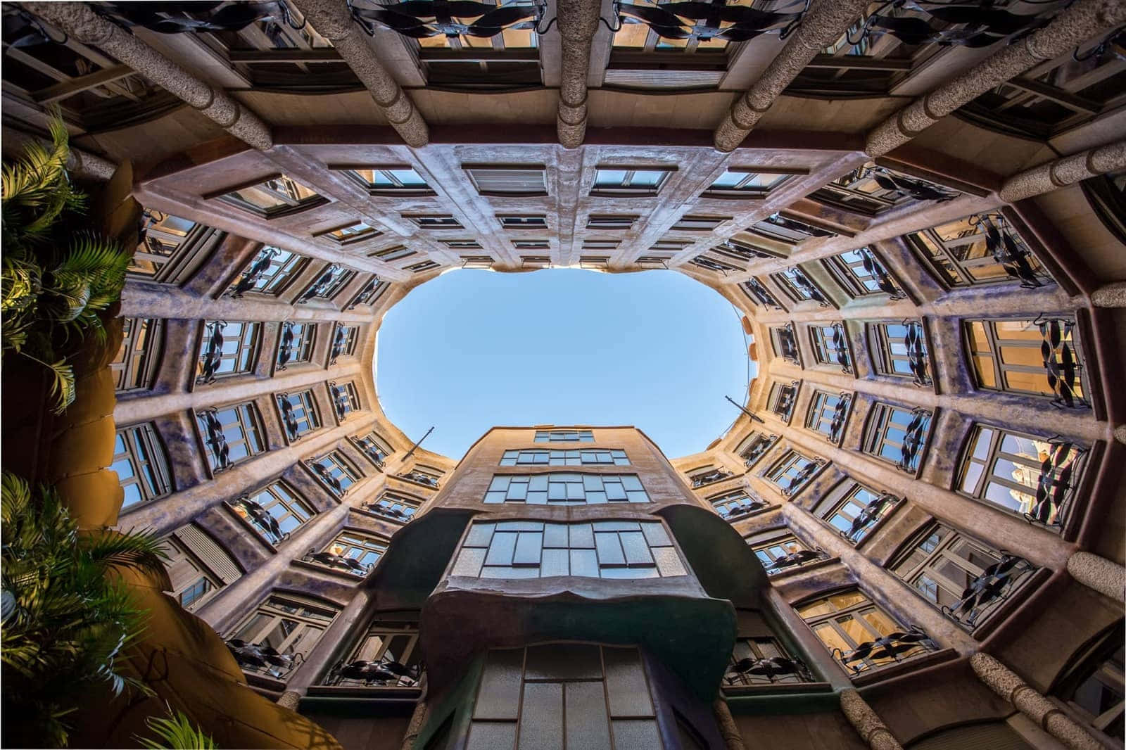 Barcelona 桌布 壁紙 — 透過彎曲的建築中庭向上仰望的戲劇性視角，展現出複雜石柱和窗戶上方清澈的藍天。