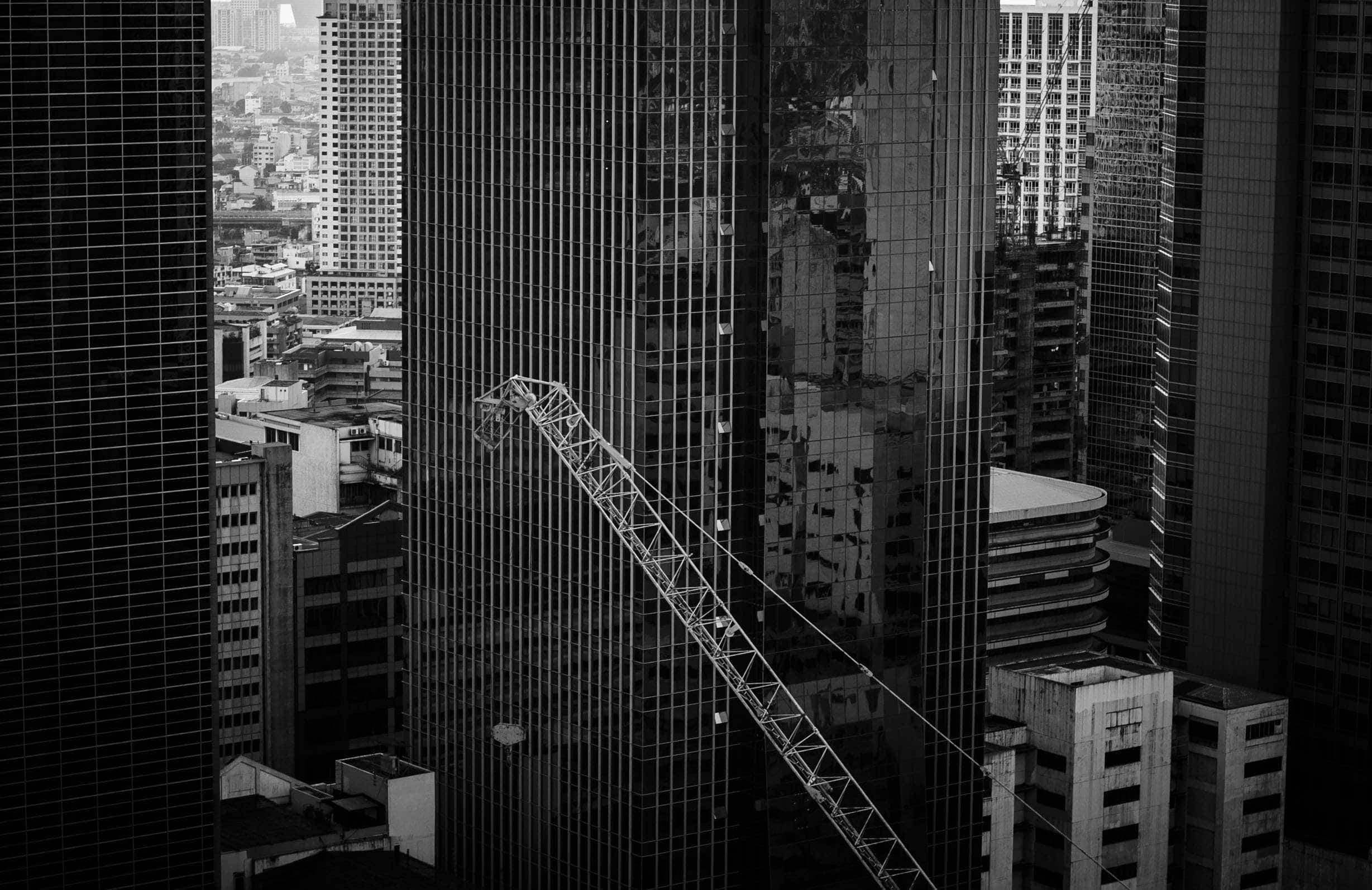 Black And White City 桌布 壁紙 — 透過摩天大樓玻璃看到的黑白城市景觀，呈現起重機與城市天際線的鮮明幾何對比。