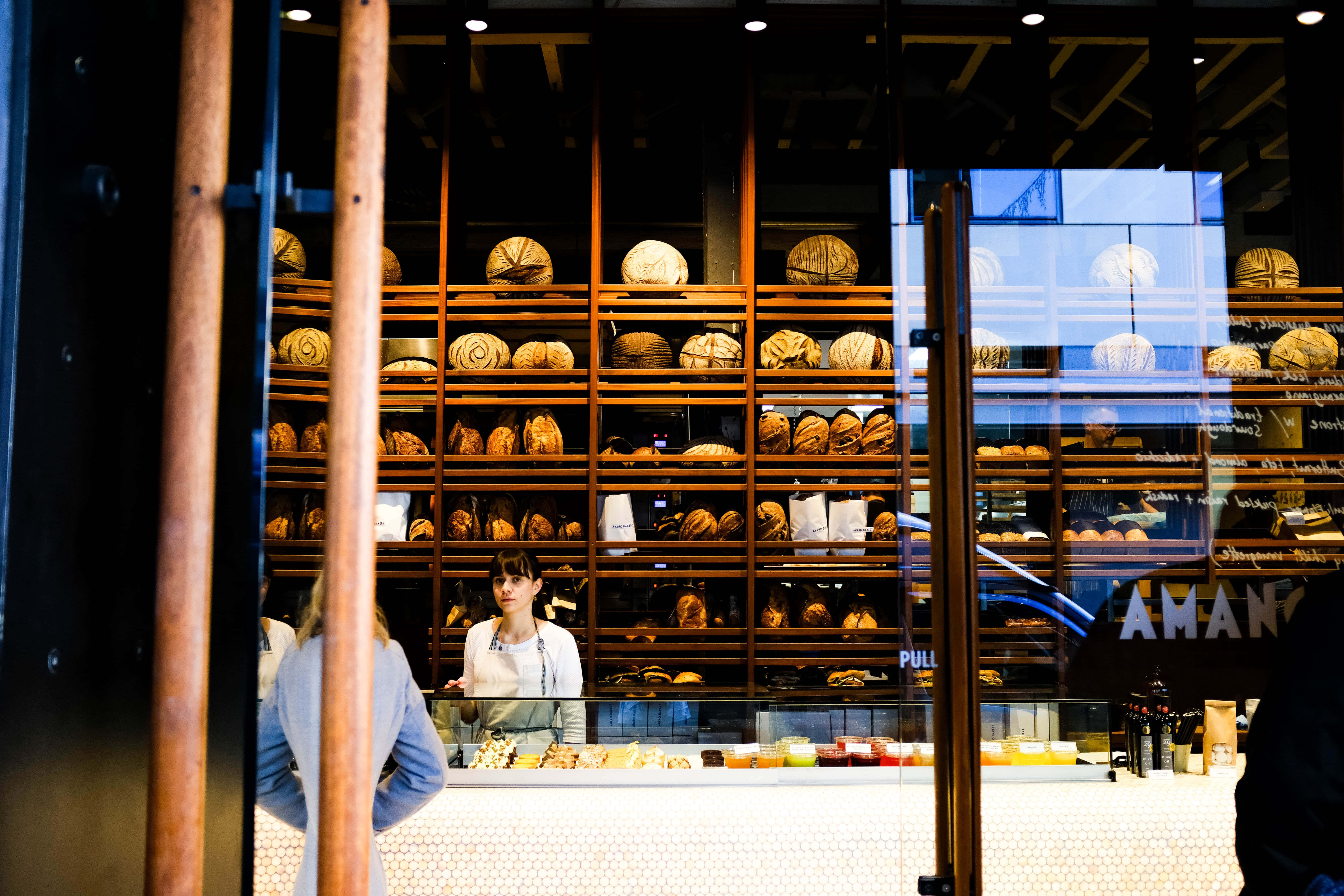 Bakery 桌布 壁紙 — 透過木柱看到的玻璃後方，裝滿金黃色麵包的麵包店展示櫃。