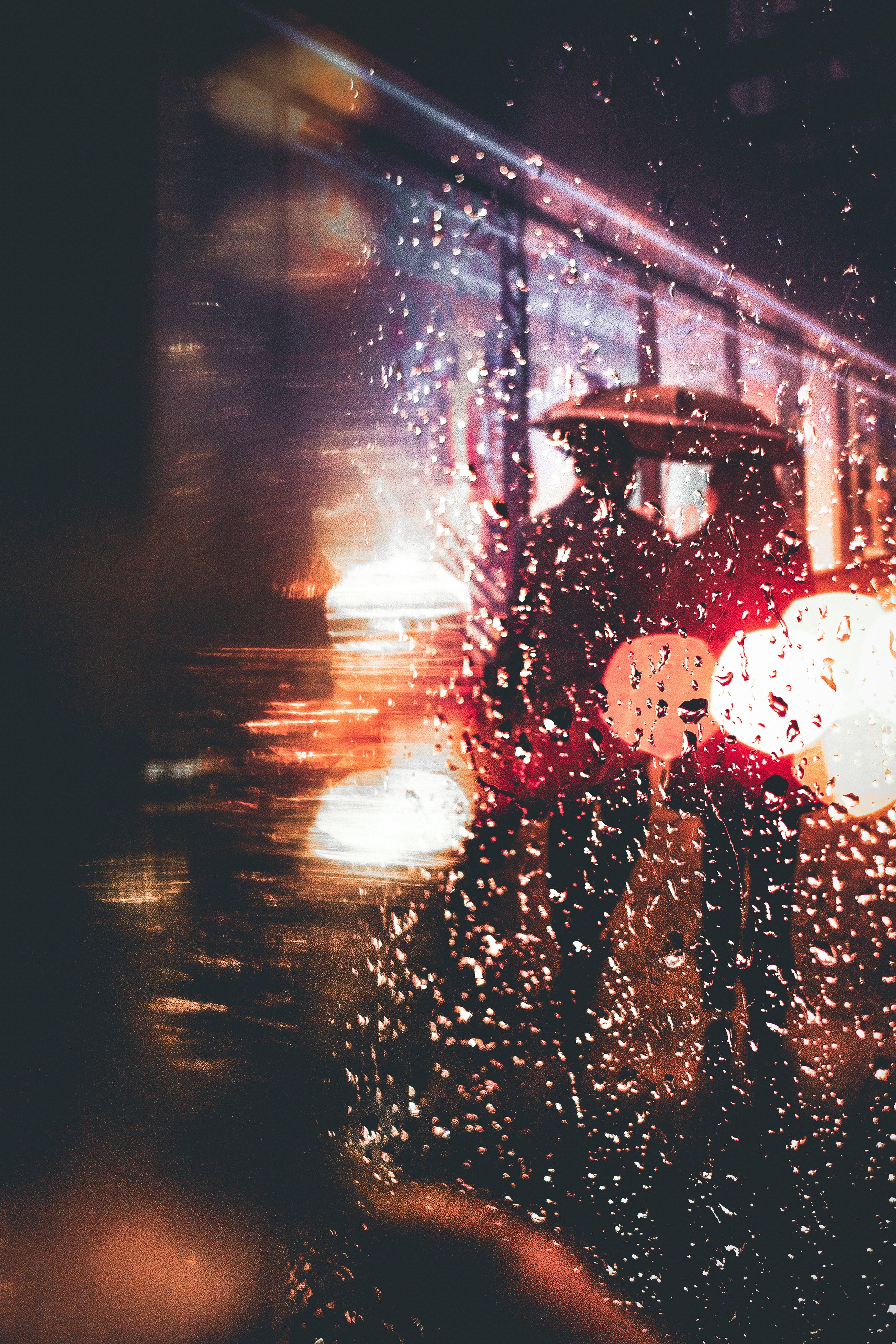 下雨 桌布 壁紙 — 透過濕窗看到的雨夜場景，模糊的城市燈光和一個撐傘的人。