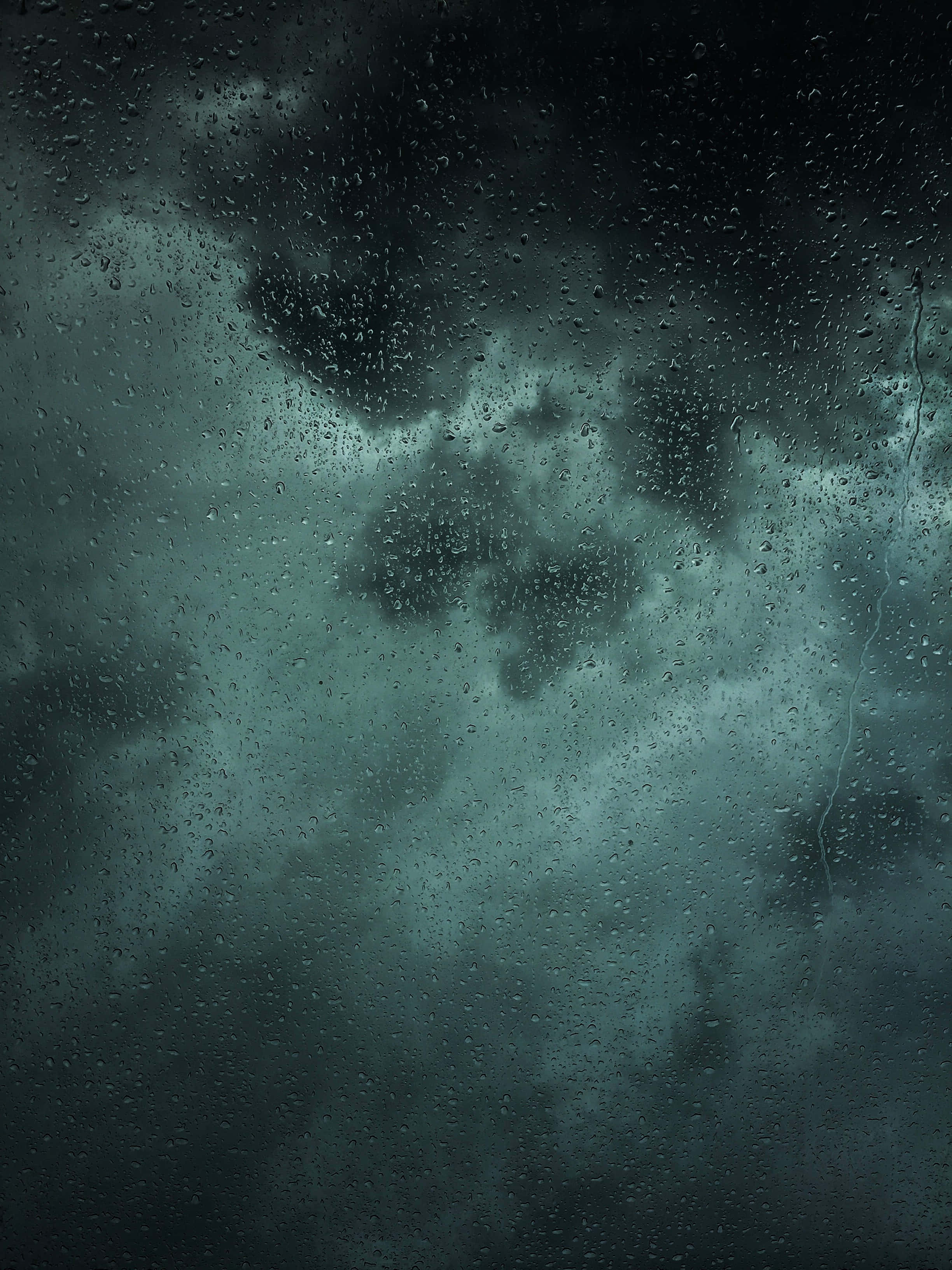 Rain 4K 桌布 壁紙 — 透過濺滿雨水的窗戶看到的深色風暴雲，帶有青綠色和灰色色調。