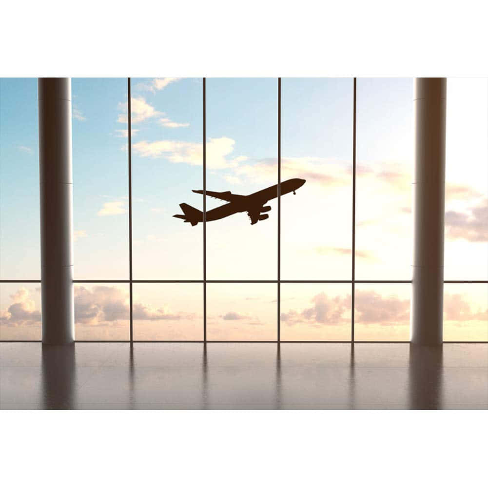 飛機 桌布 壁紙 — 透過現代機場航廈窗戶看到的客機在日落天空飛行的剪影。