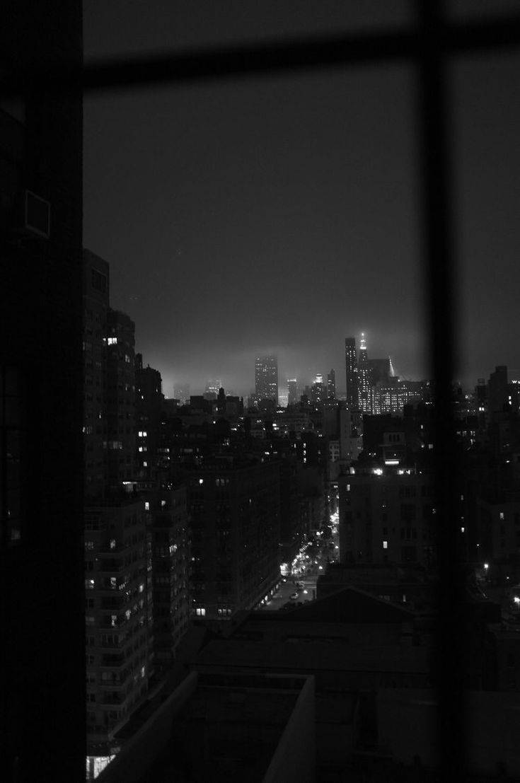 Monochrome 桌布 壁紙 — 透過窗框看到的單色夜景城市景觀，發光的燈光穿透霧氣瀰漫的天際線。