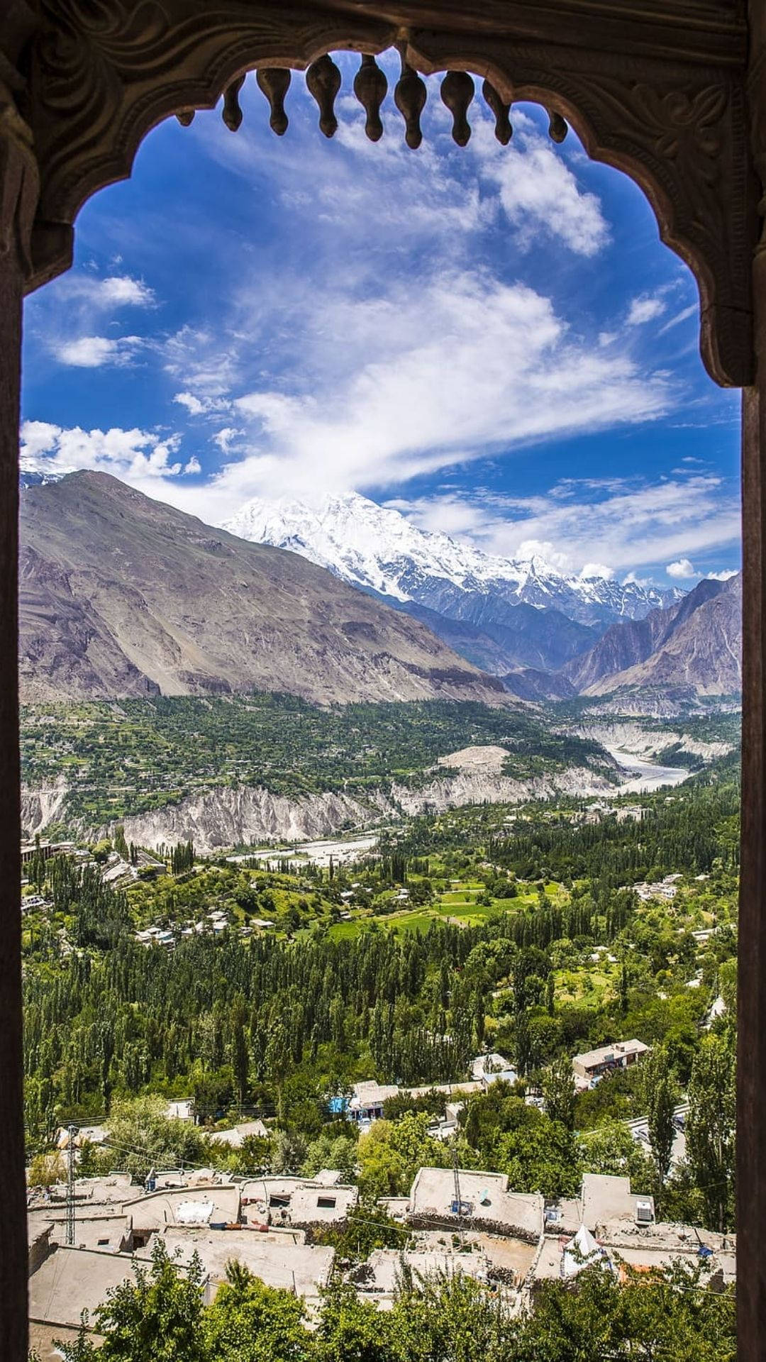 Pakistan 桌布 壁紙 — 透過裝飾華麗的拱形窗戶，可以看到一片鬱鬱蔥蔥的山谷，坐落在高聳的雪山之間，頭頂是明亮的藍天。