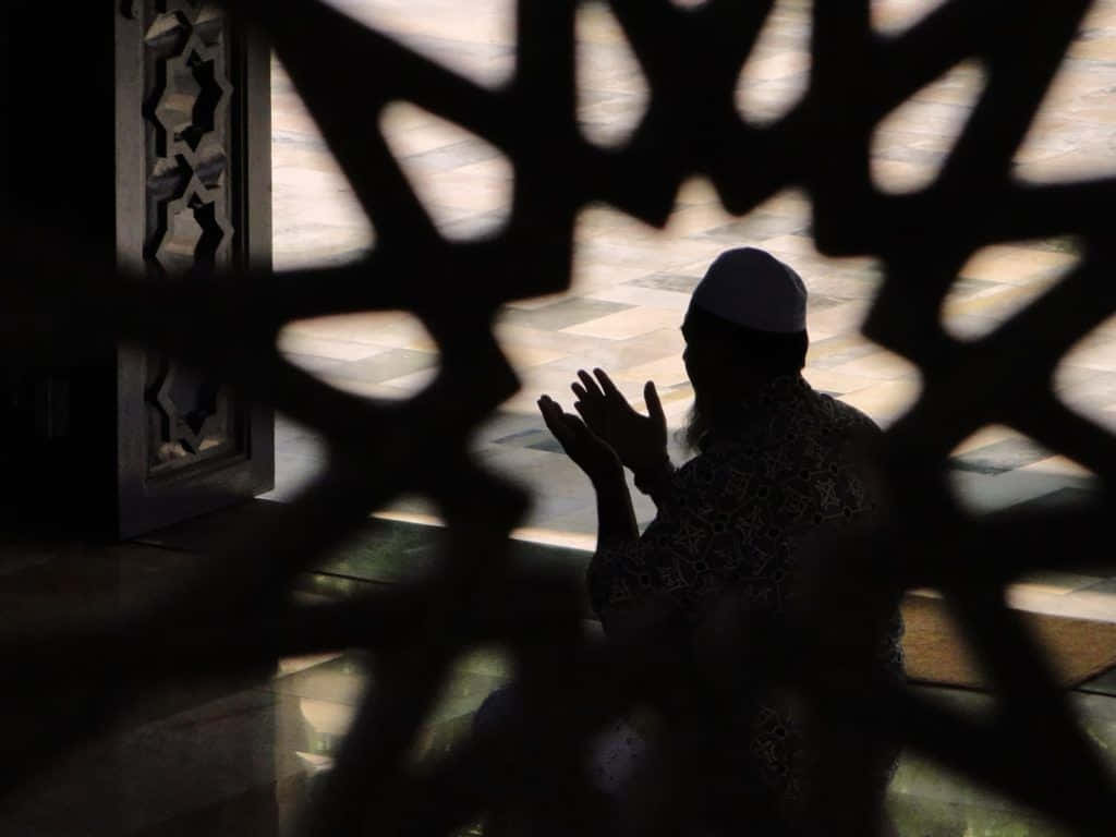 Praying 桌布 壁紙 — 透過複雜幾何格子看到的祈禱人物剪影，在瓷磚地板上投下斑駁陰影。