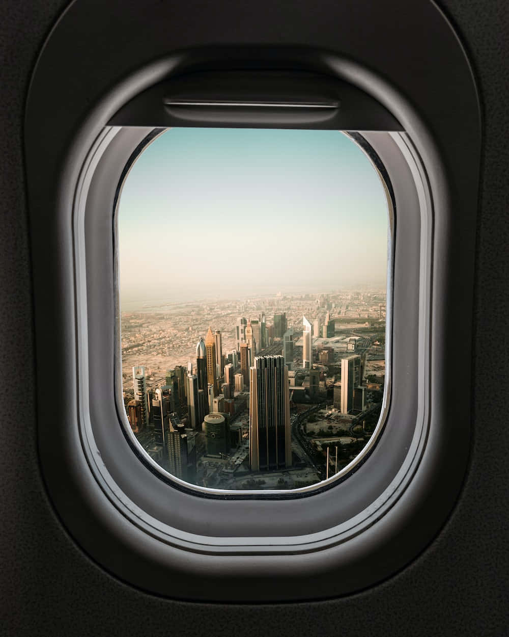 Airplane Window 桌布 壁紙 — 透過飛機窗戶看到的現代城市天際線的空中景觀，帶有柔和的金色光線。