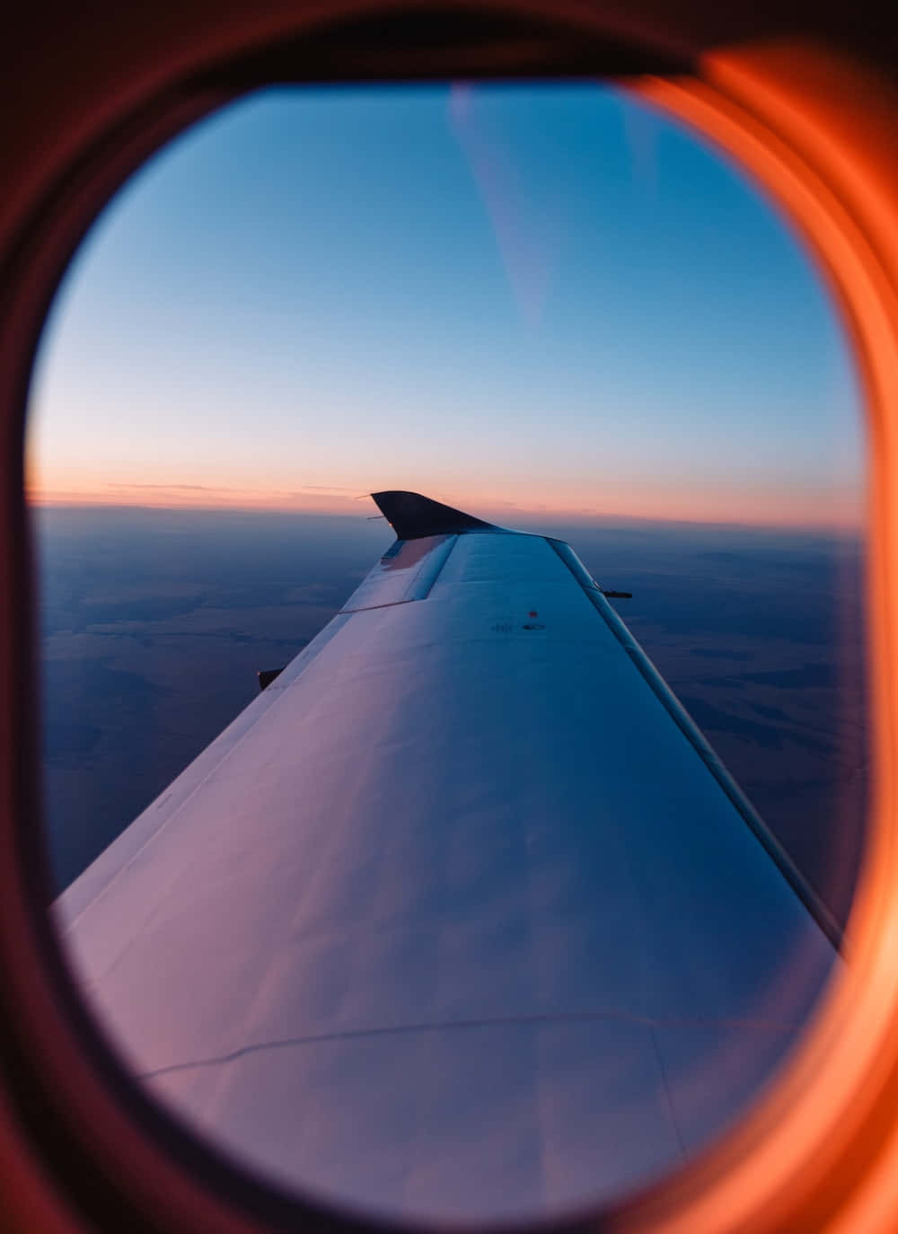 Airplane Window 桌布 壁紙 — 透過飛機窗戶看到的飛機機翼，夕陽西下，帶有橙色邊緣和漸變天空。