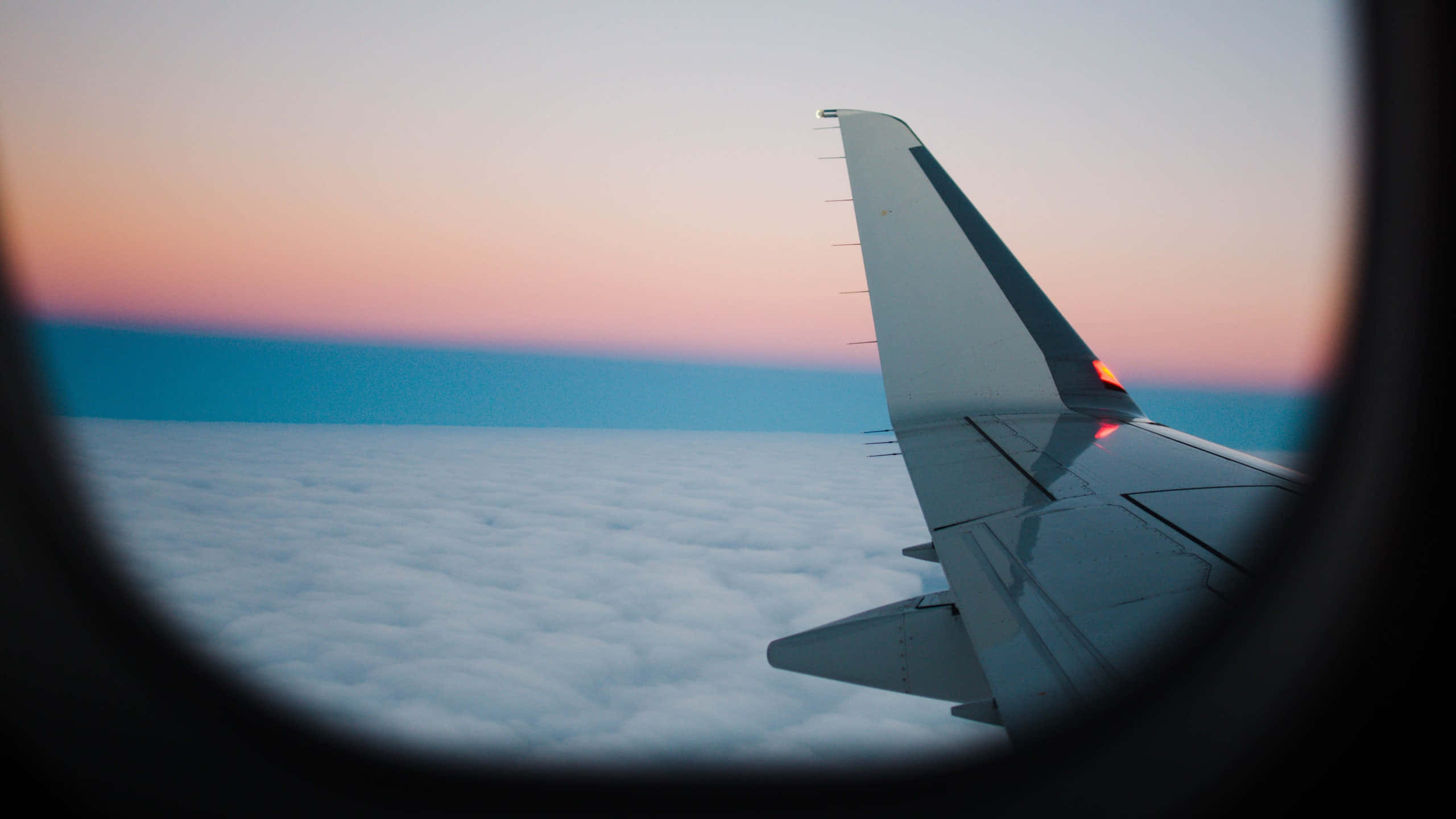 window 桌布 壁紙 — 透過飛機窗戶看到的飛機機翼，夕陽西下，粉橙色天空，蓬鬆白雲之上。