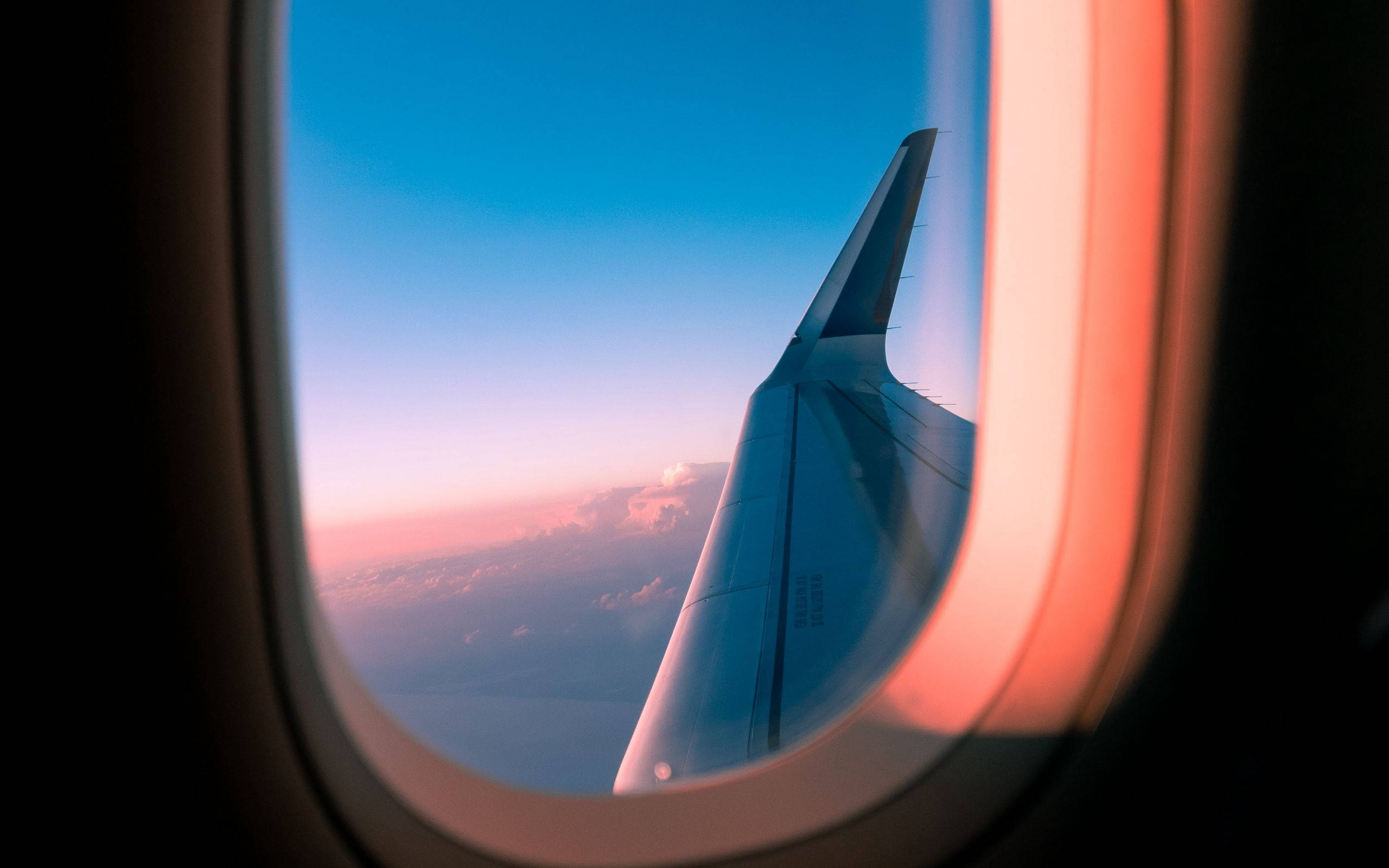 天空景色 桌布 壁紙 — 透過飛機窗戶看到的飛機機翼，日落時分，粉紅色和藍色的天空，下方有雲。