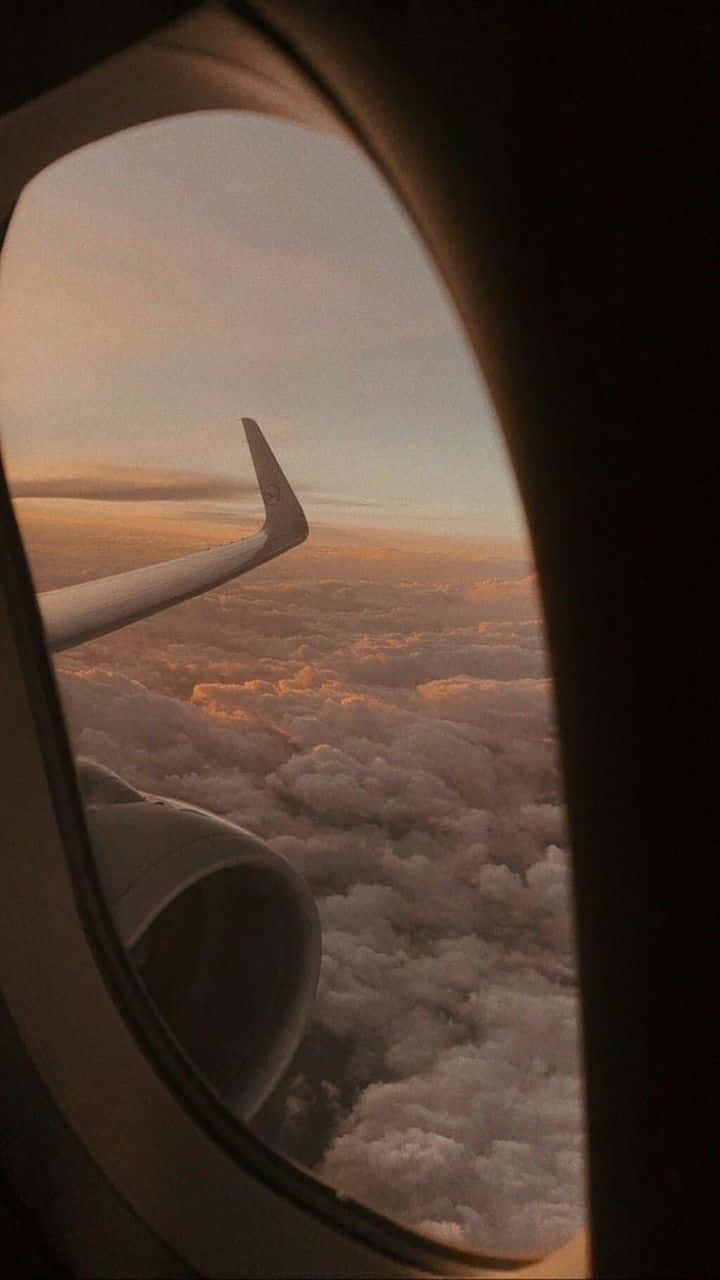 飛機 桌布 壁紙 — 透過飛機窗戶看到金色日落雲層上的飛機機翼和引擎。