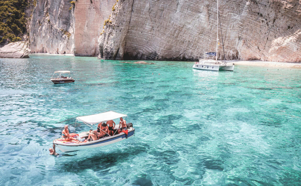 Greek Island 桌布 壁紙 — 遊客在清澈碧綠的海水中，被高聳的白色懸崖環繞，於小船上放鬆身心。