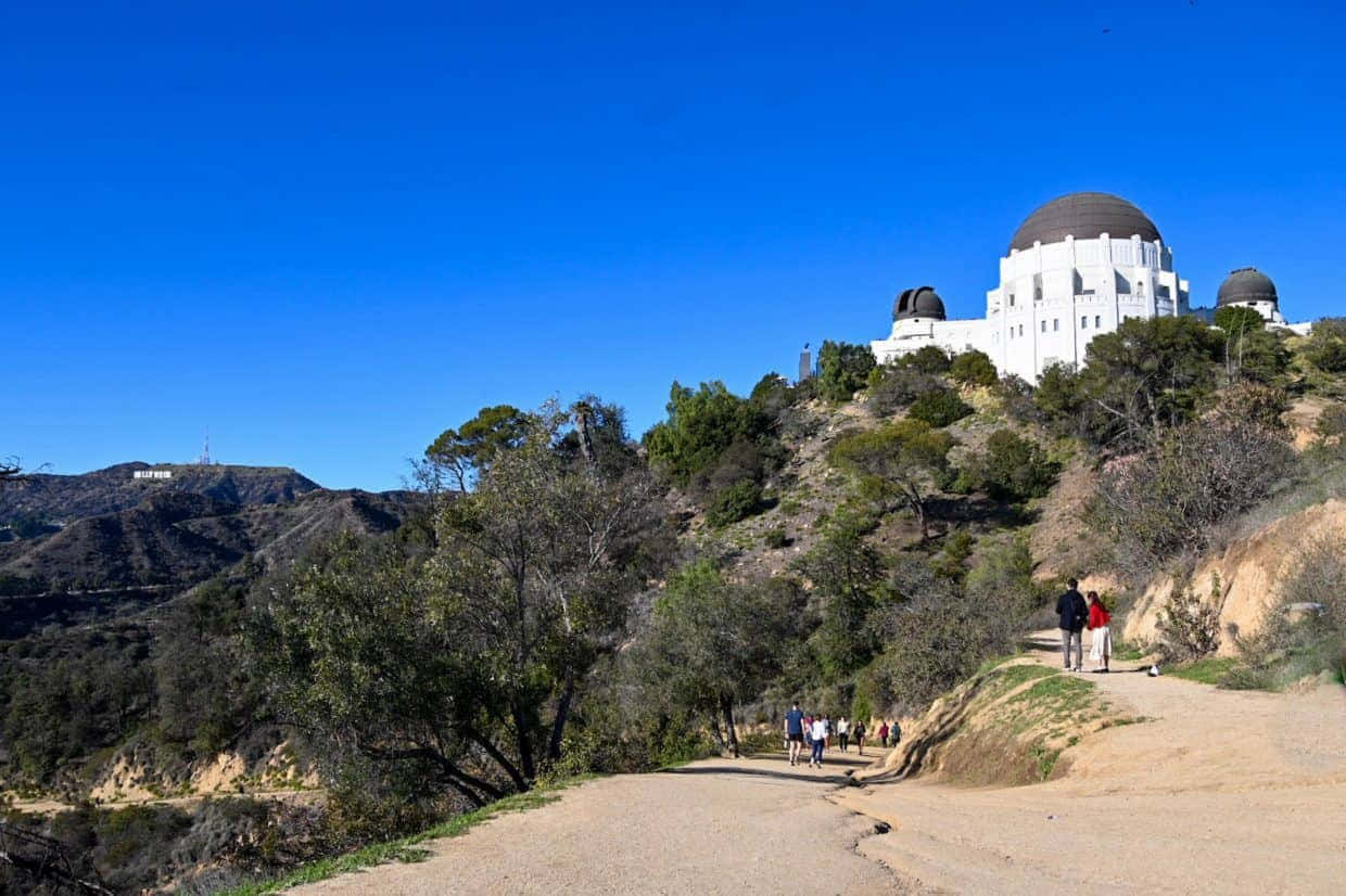 Observatory 桌布 壁紙 — 遊客沿著陽光普照的泥土小徑漫步，前往坐落在山頂上、藍天白雲下的標誌性格里菲斯天文台。
