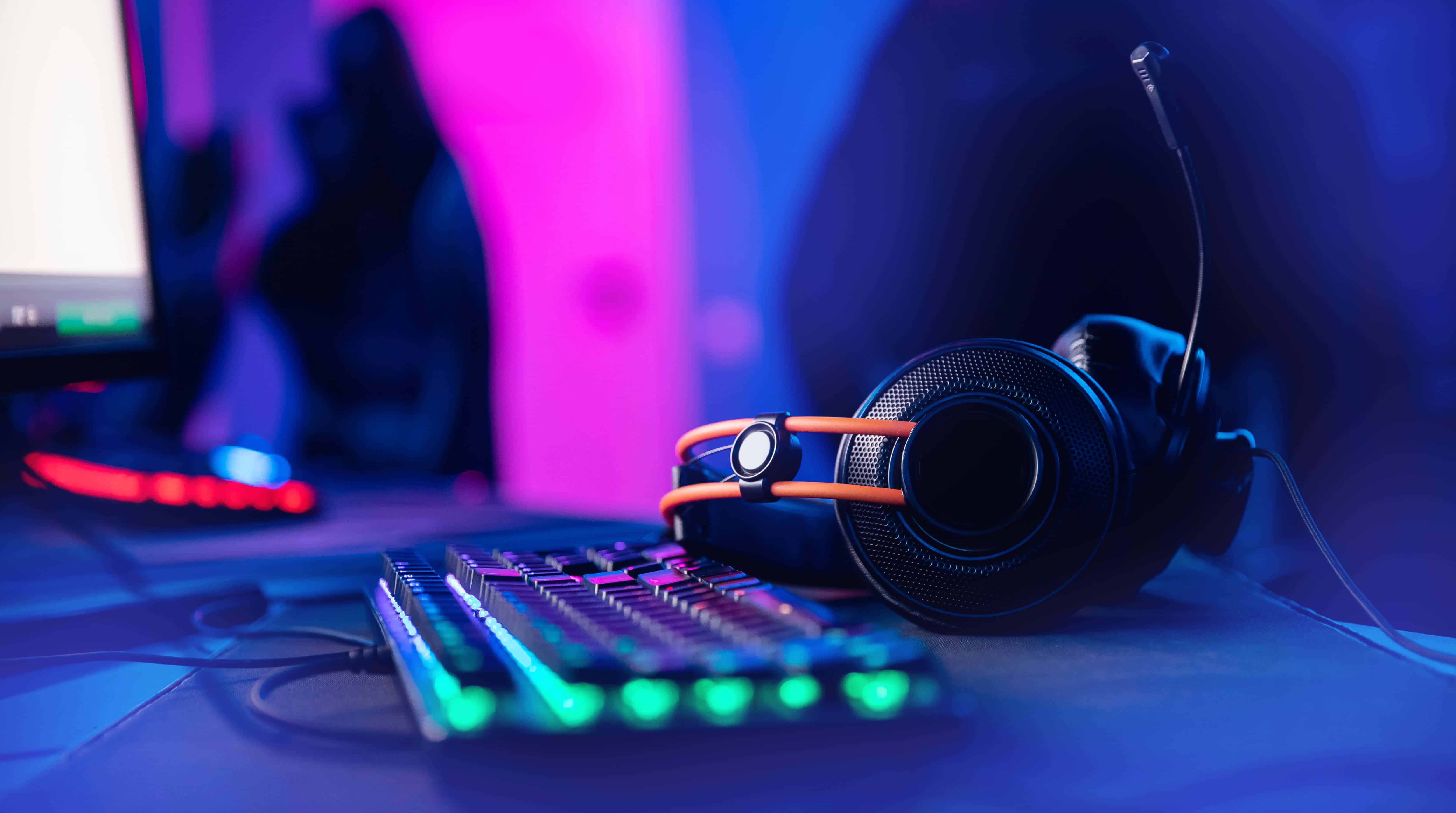 Gaming Headsets 桌布 壁紙 — 遊戲耳機和鍵盤在紫色和藍色環境燈光下，於桌上散發出鮮豔的霓虹光芒。