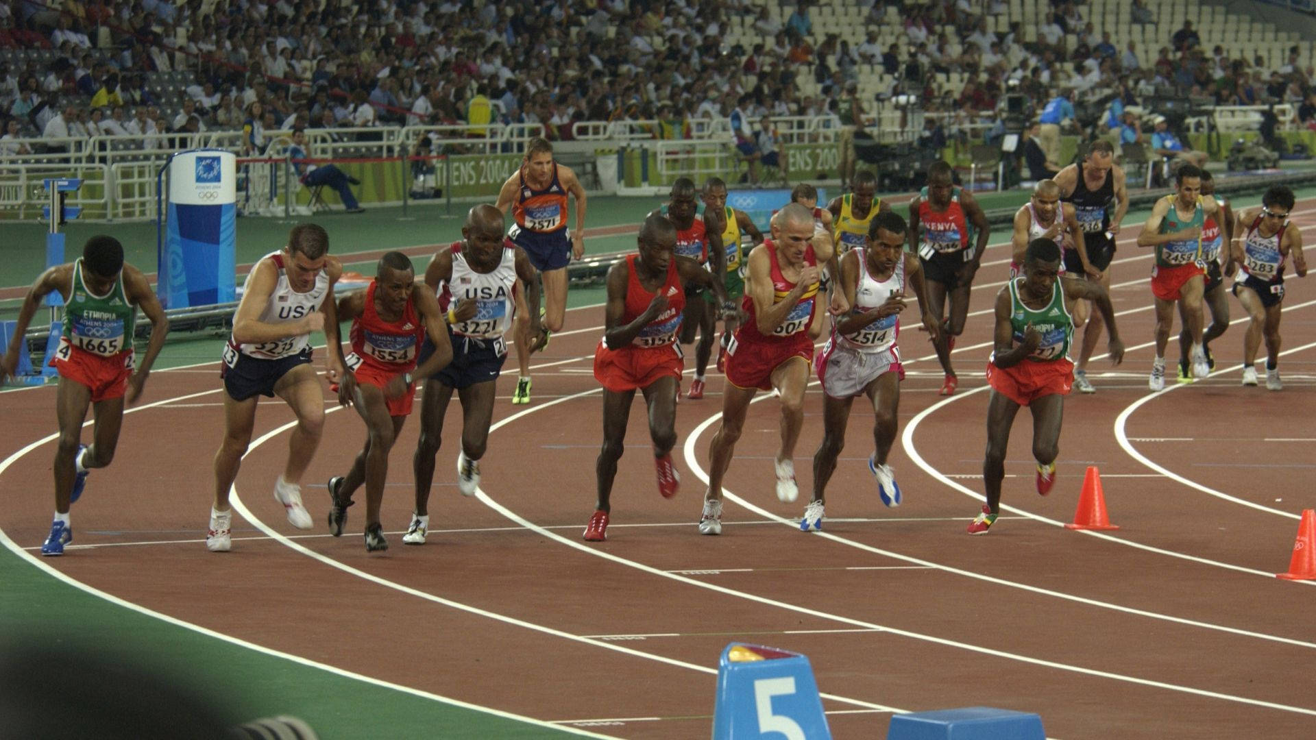 Olympics 桌布 壁紙 — 運動員在紅色跑道上激烈衝刺，觀眾在奧運比賽期間從體育場看台歡呼。