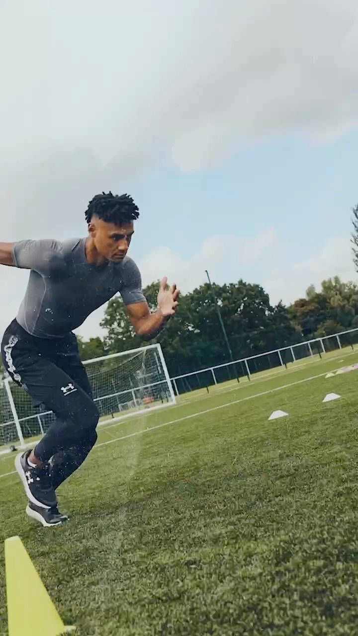 Football Field 桌布 壁紙 — 運動員在綠色草地上低身衝刺穿過雨滴，背景有白色錐體和球門網。