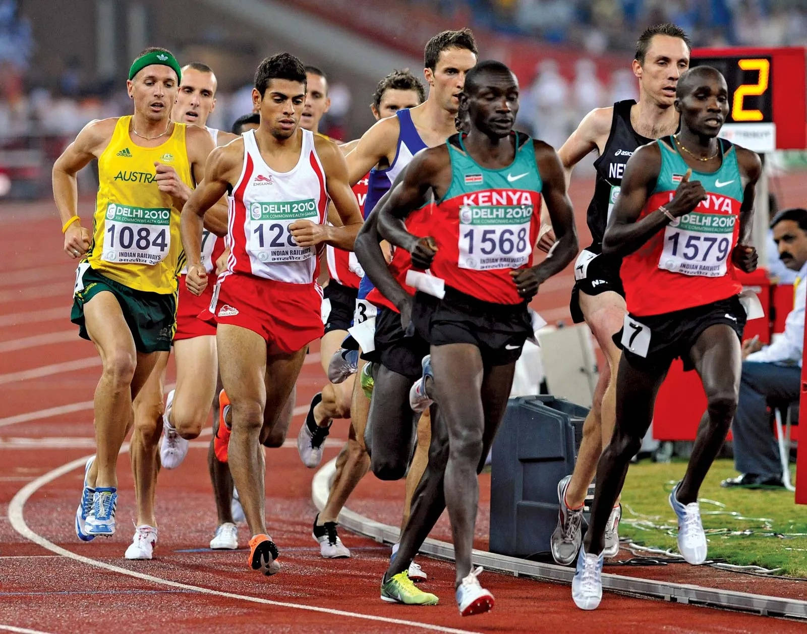 Athletics 桌布 壁紙 — 運動員穿著鮮豔的制服在體育場燈光下於紅色跑道上激烈衝刺進行競賽。