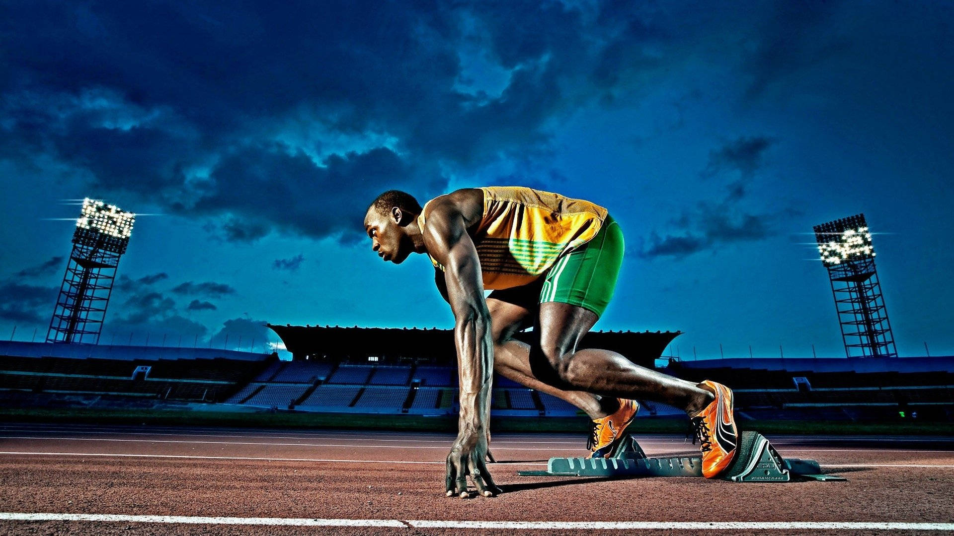 Athletic 桌布 壁紙 — 運動員身穿黃綠色制服，在戲劇性的藍色暮色天空下，蹲在跑道上的起跑器上，體育場燈光閃爍。