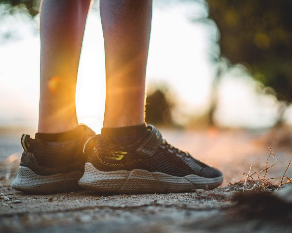 Skechers 桌布 壁紙 — 運動鞋在泥地上的特寫，溫暖的金色陽光在腿後閃耀。