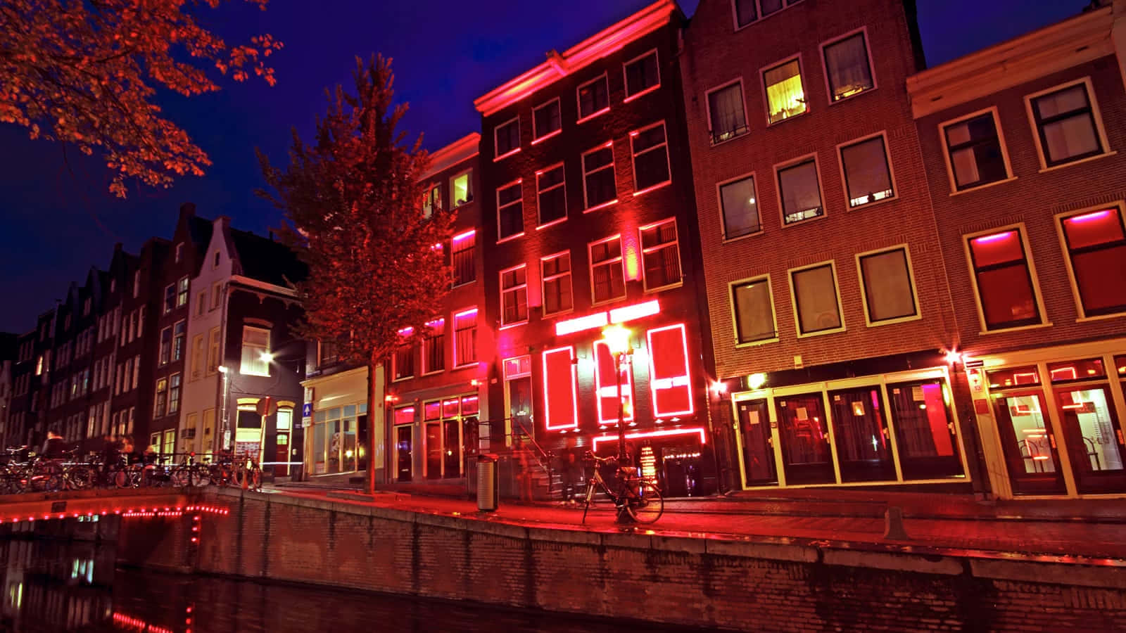 Red Light District 桌布 壁紙 — 運河旁充滿活力的夜景，紅色霓虹燈光倒映在水面和歷史磚砌建築上。