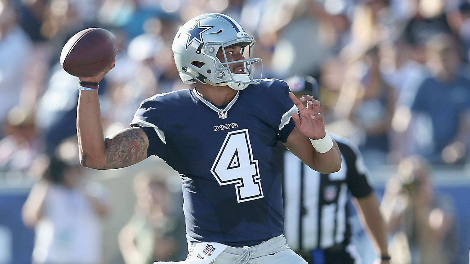 Dak Prescott 桌布 壁紙 — 達拉斯牛仔隊四分衛4號身穿海軍藍球衣，在日間比賽中準備投擲橄欖球，背景是模糊的體育場人群。