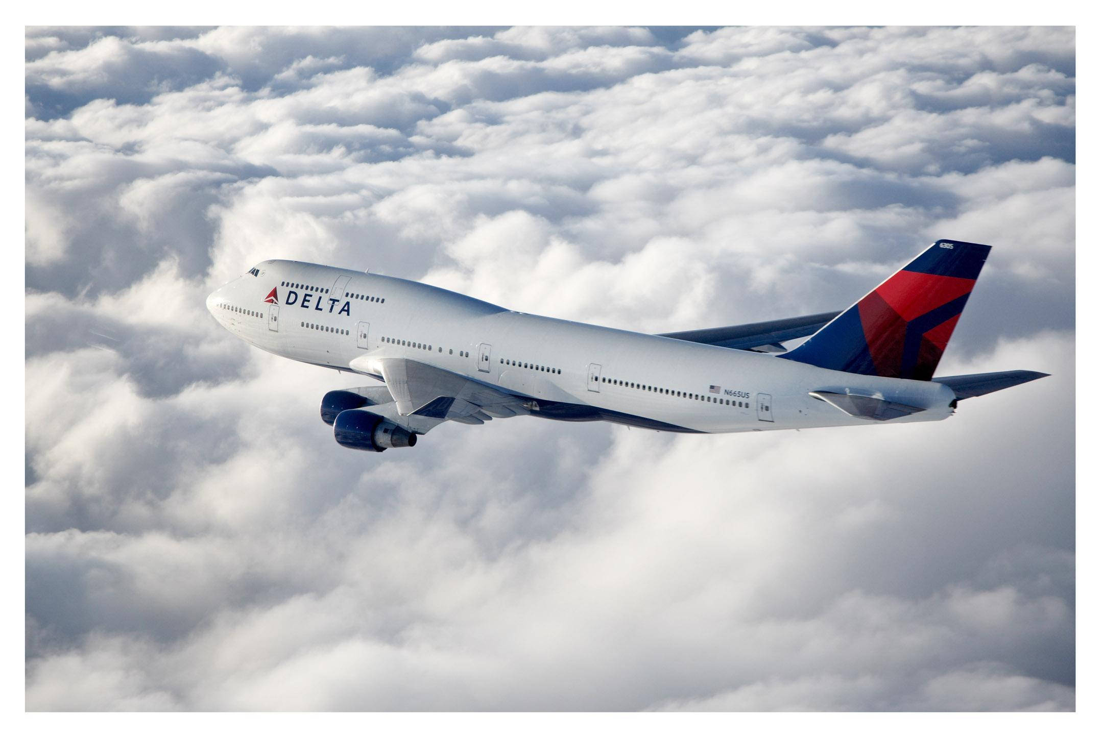飛機 桌布 壁紙 — 達美航空的波音747在明亮的天空下，優雅地翱翔於廣闊的蓬鬆白雲之上。
