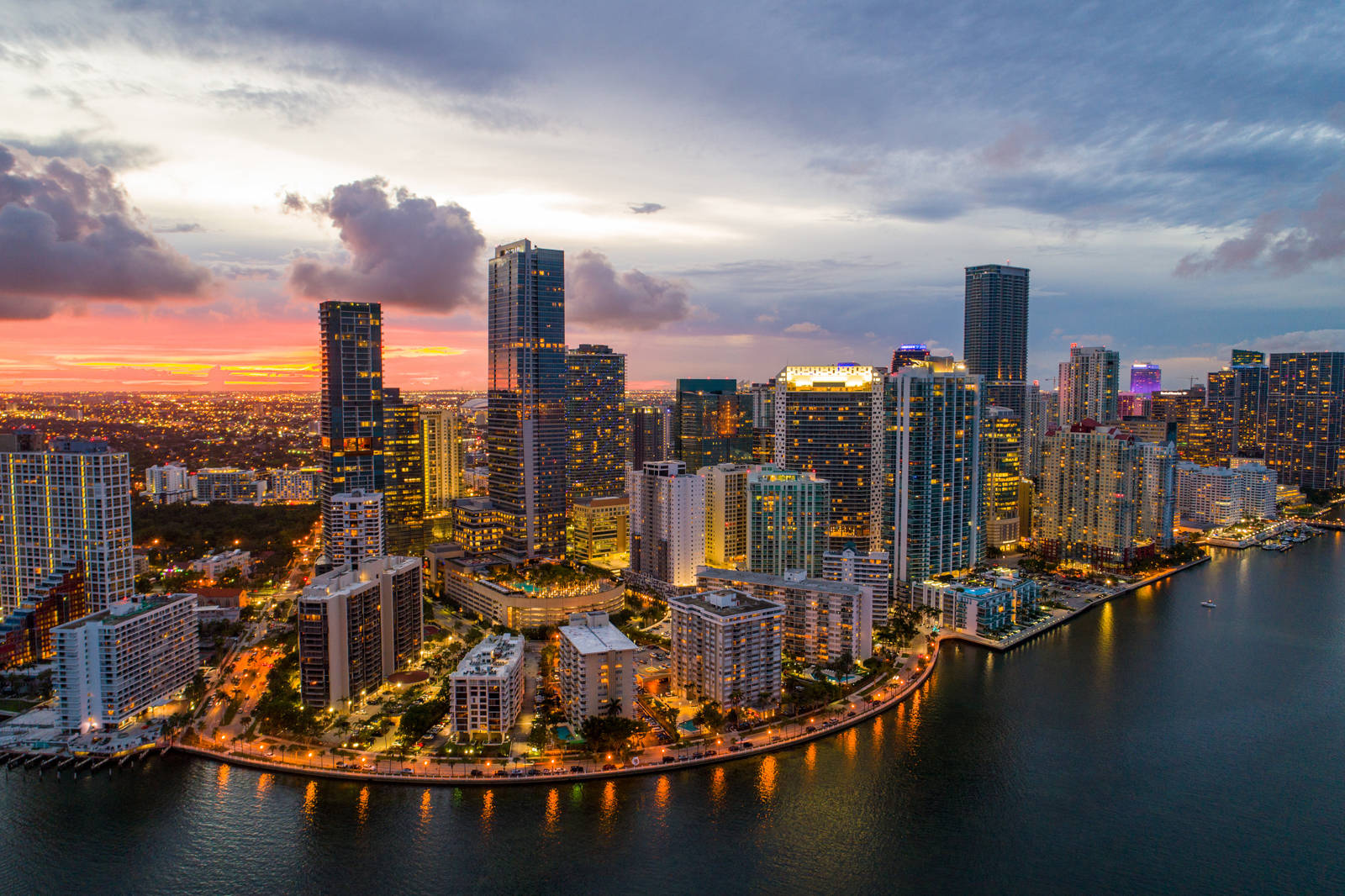 Miami 桌布 壁紙 — 邁阿密天際線的鳥瞰圖，夕陽下發光的摩天大樓在粉紅色、橙色和紫色雲層下的水面上反射。