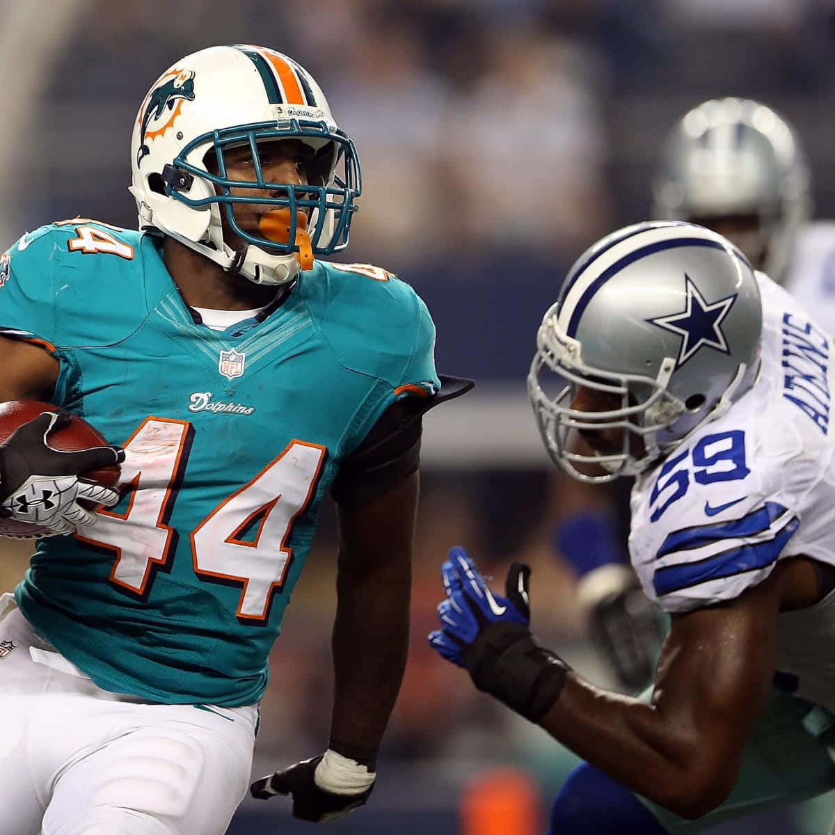 Fantasy Football Profile 桌布 壁紙 — 邁阿密海豚隊44號球員在夜間比賽中帶著橄欖球奔跑，達拉斯牛仔隊的防守球員正在逼近。