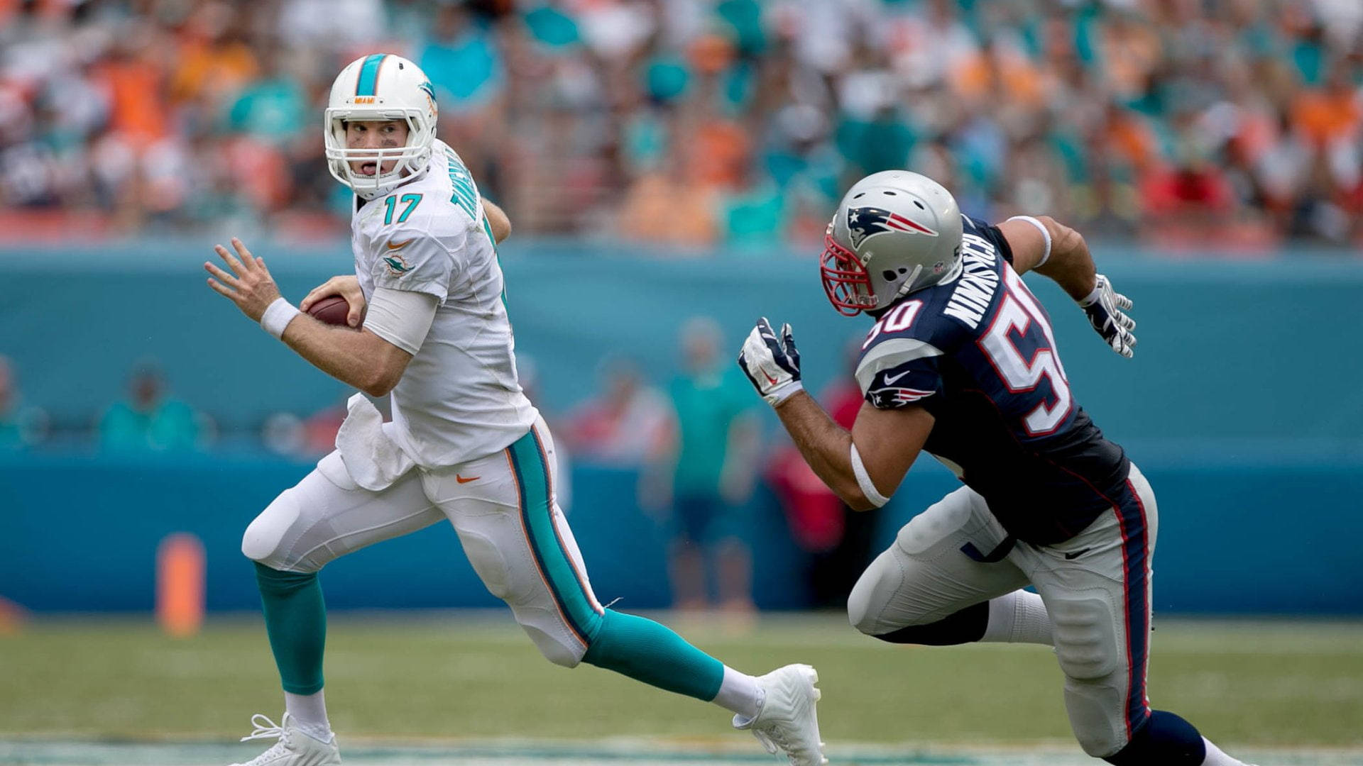 dolphins 桌布 壁紙 — 邁阿密海豚隊的四分衛持球衝刺，而新英格蘭愛國者隊的線衛在日間NFL比賽中逼近。
