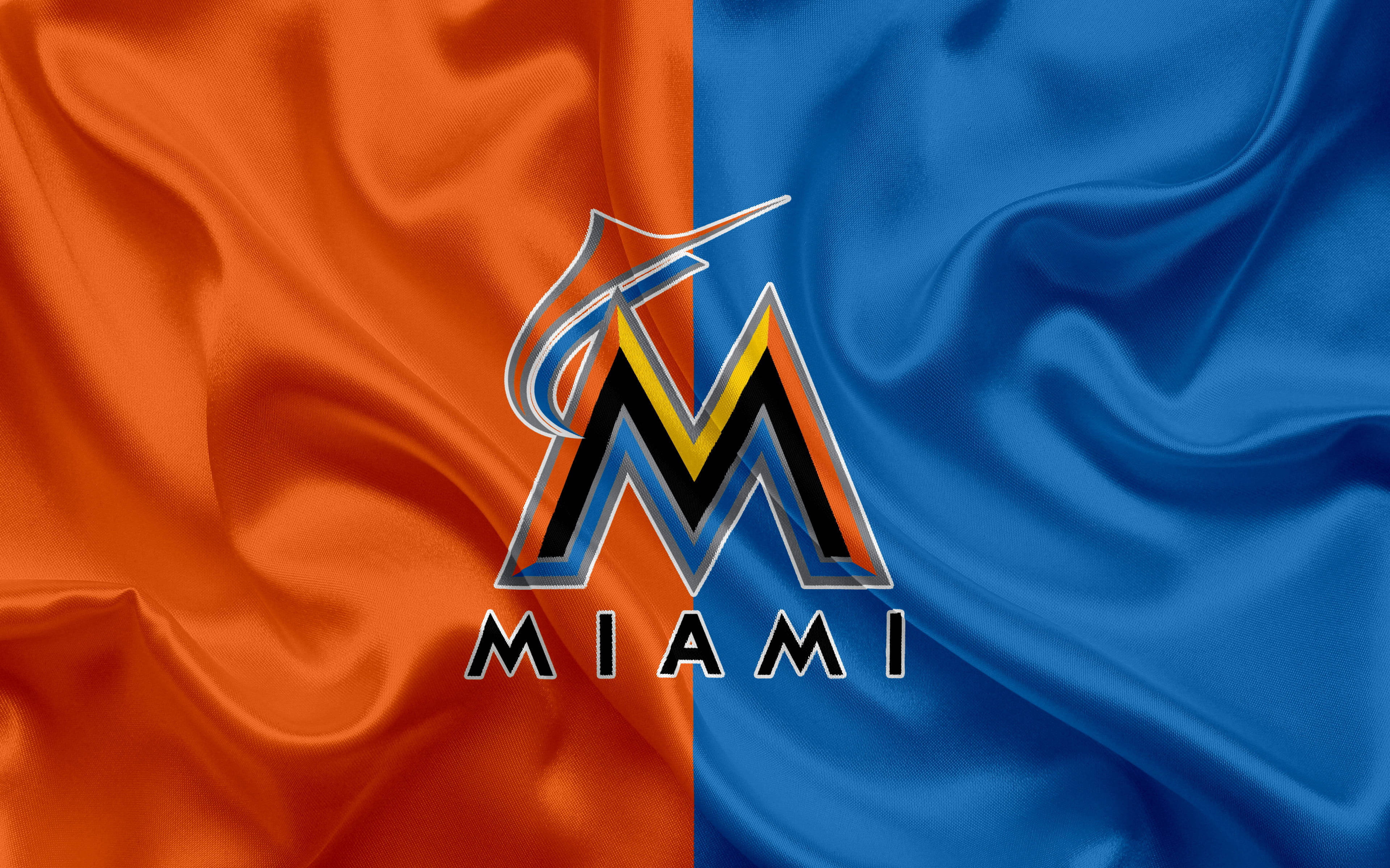 Marlins 桌布 壁紙 — 邁阿密馬林魚標誌居中，背景為橙色和藍色緞面布料，帶有流暢的褶皺。