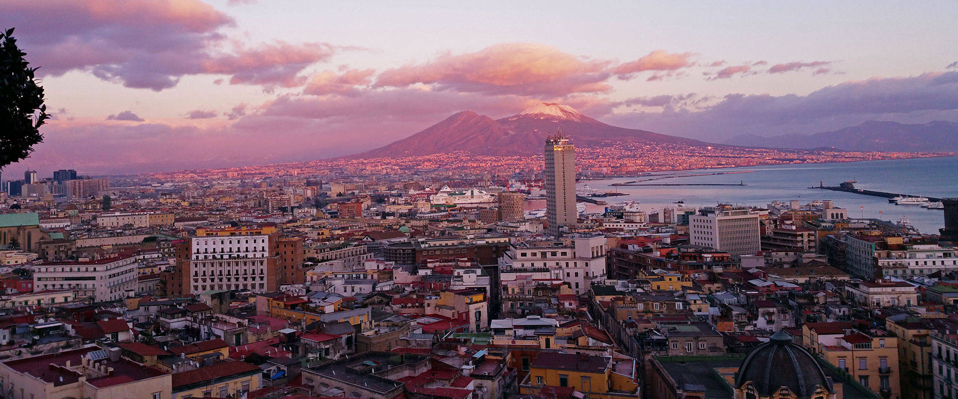 Naples 桌布 壁紙 — 那不勒斯的全景日落景觀，維蘇威火山聳立於城市和海洋之上。