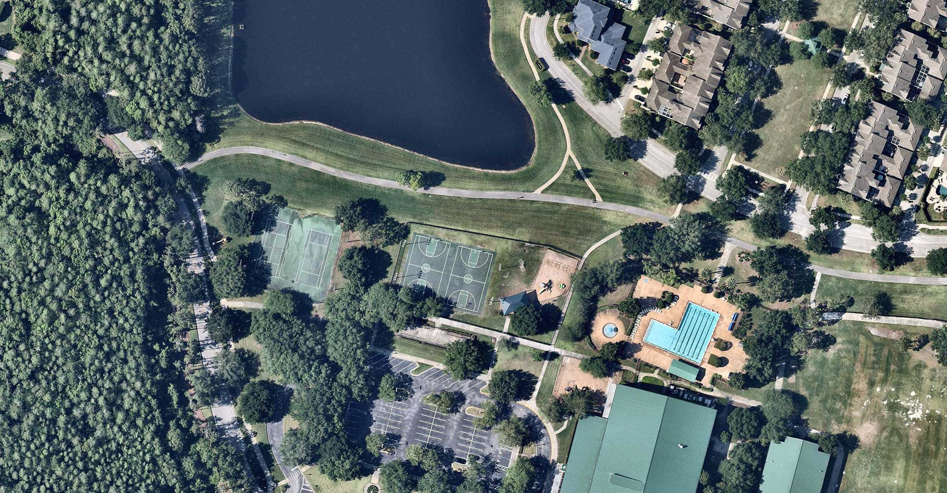 Village 桌布 壁紙 — 郊區公園的鳥瞰圖，設有網球場、籃球場和游泳池，周圍環繞著樹木和房屋。