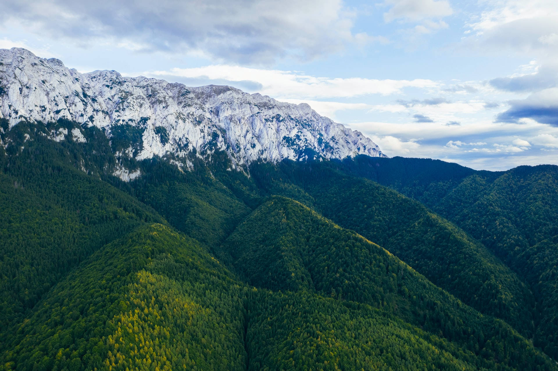 Mountain Landscape 桌布 壁紙 — 部分多雲的天空下，鬱鬱蔥蔥的綠色森林山脈和白雪覆蓋的山峰的鳥瞰圖。