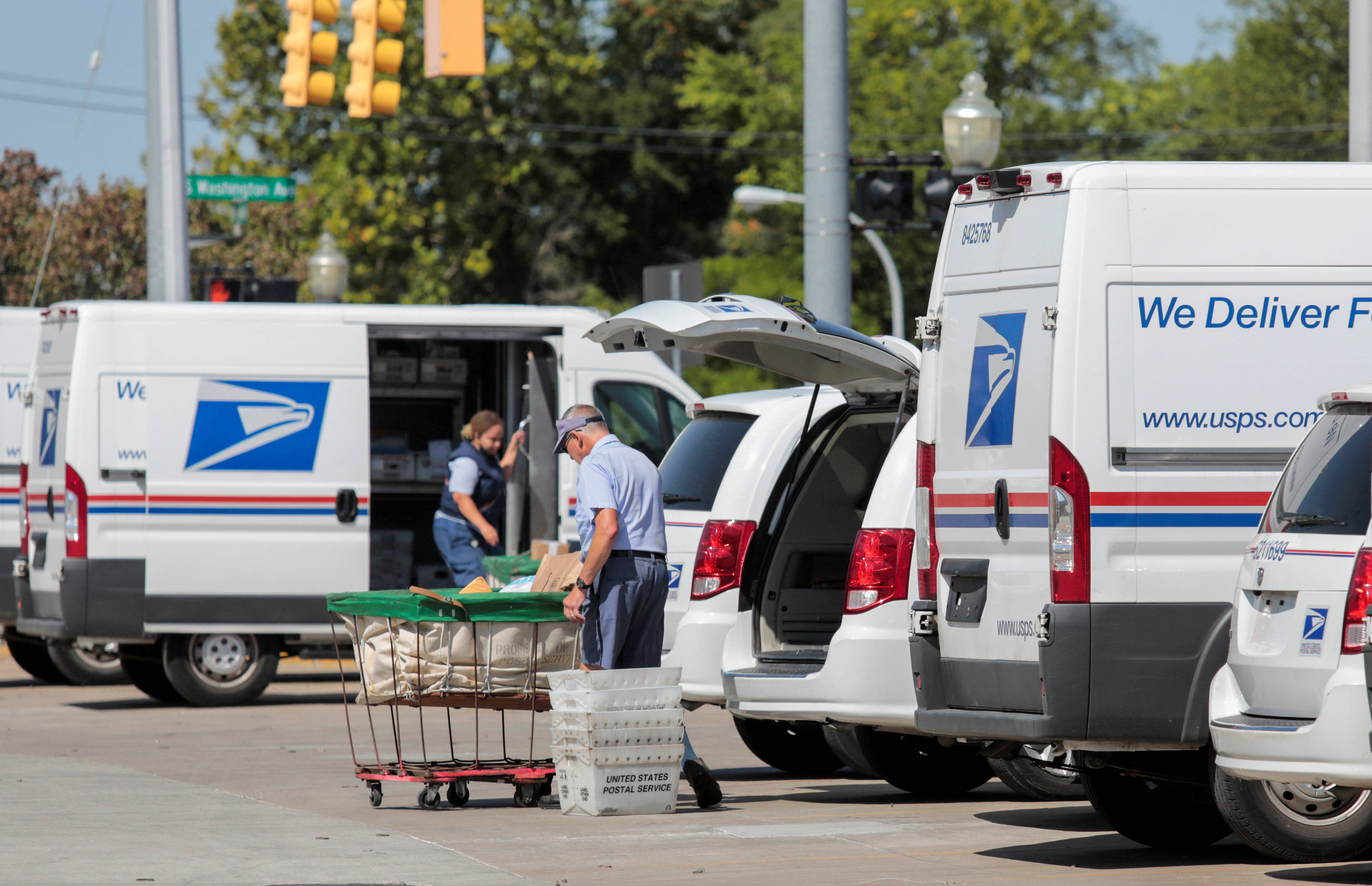 Usps 桌布 壁紙 — 郵政工作人員在晴朗的天空下，在繁忙的城市配送場地從白色USPS貨車上卸下郵件。